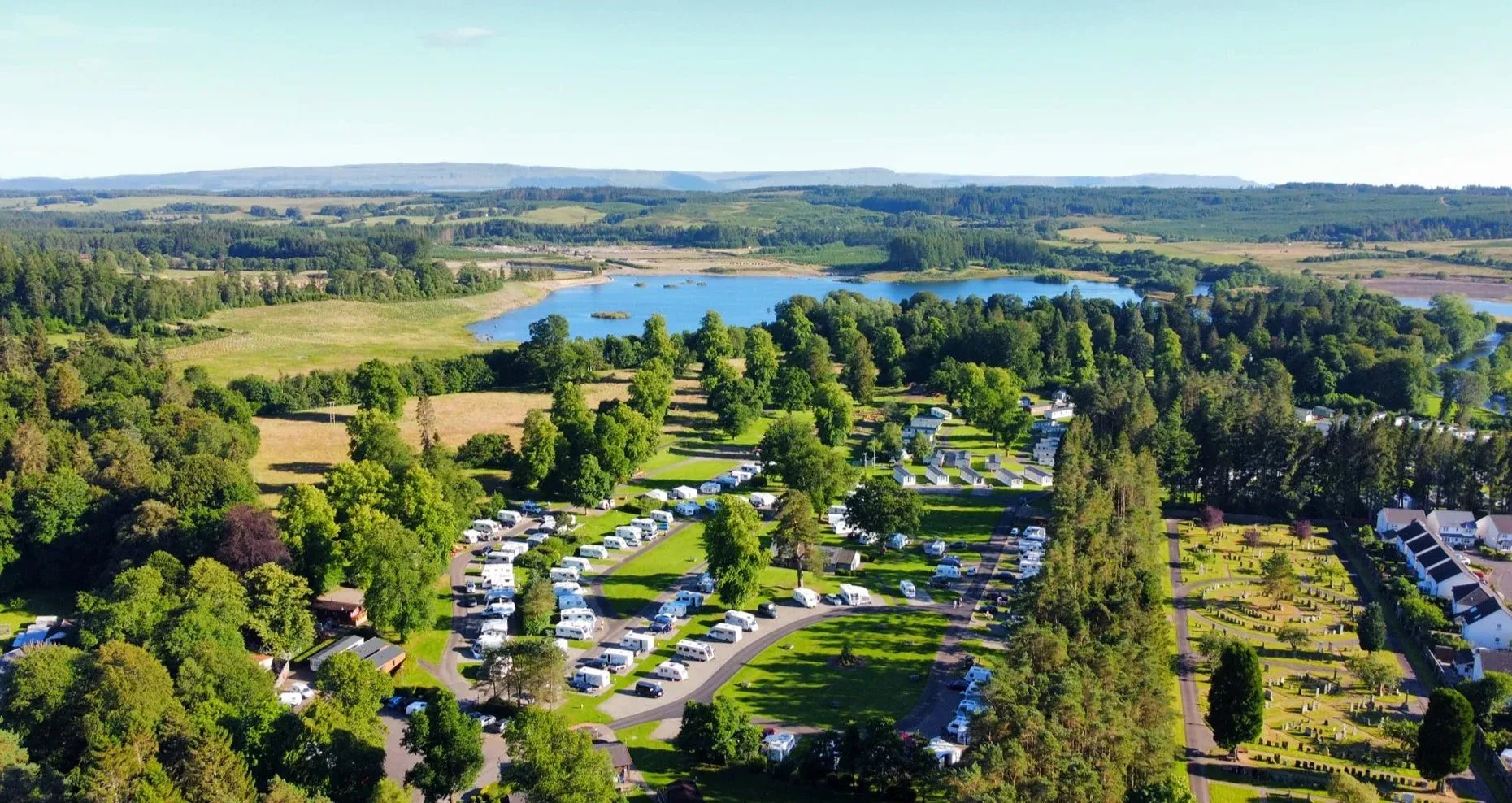 Aerial view of Callander Woods Holiday Park with caravans and a lake in the background.
