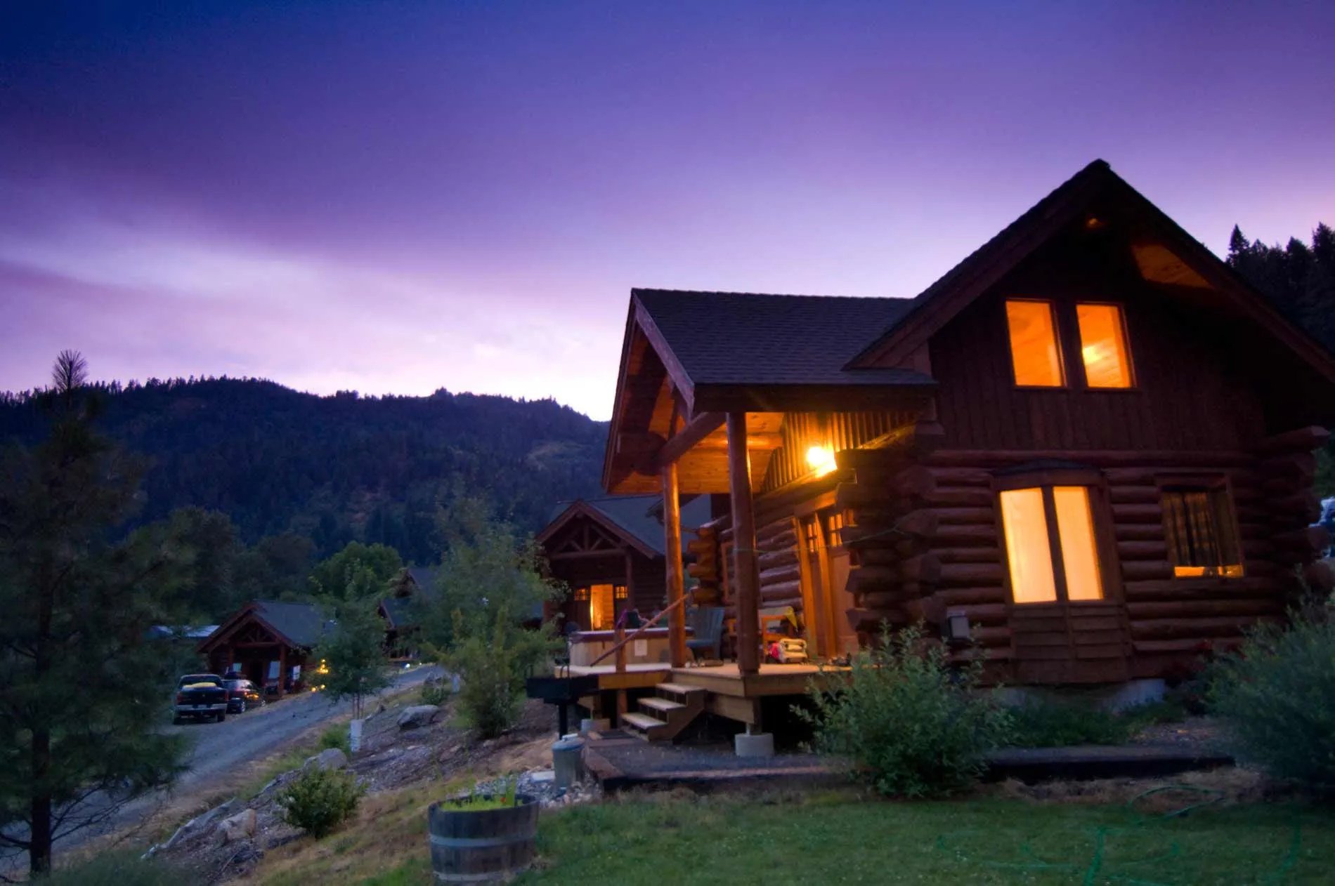 Illuminated log cabin exterior at dusk, with warm lights glowing from windows and porch.