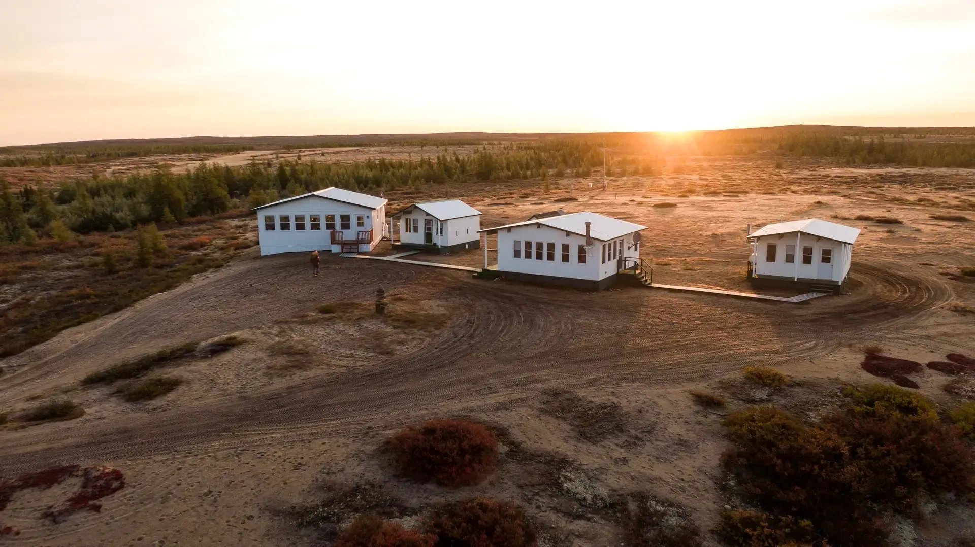 Aerial view of white cabins on a rise at sunset, with golden light on the horizon