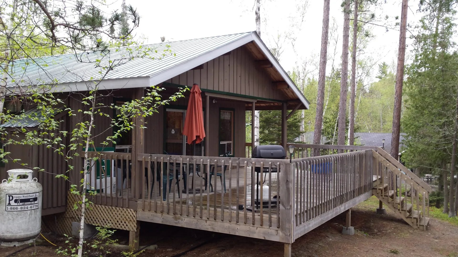 Brown cabin exterior with a green roof and a large wooden deck overlooking the woods.