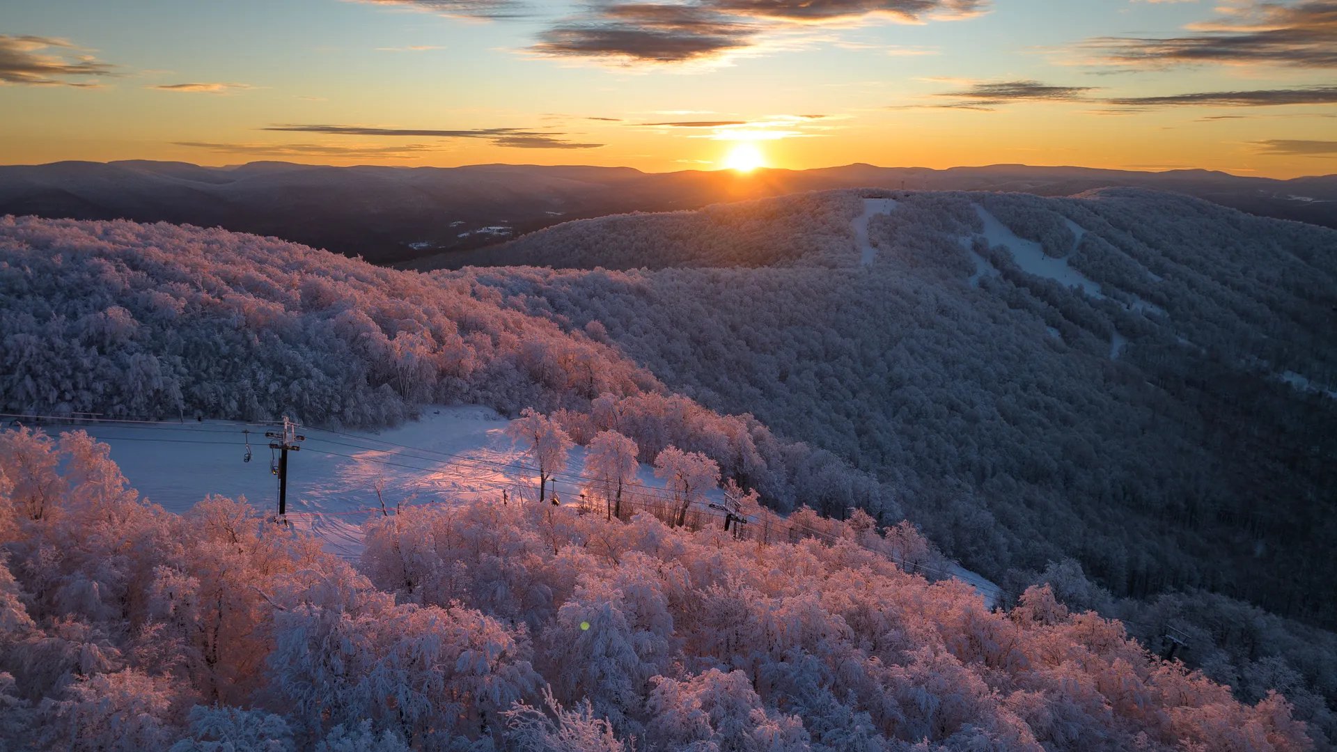 Aerial view of snowy mountain peaks at sunset with an orange glow