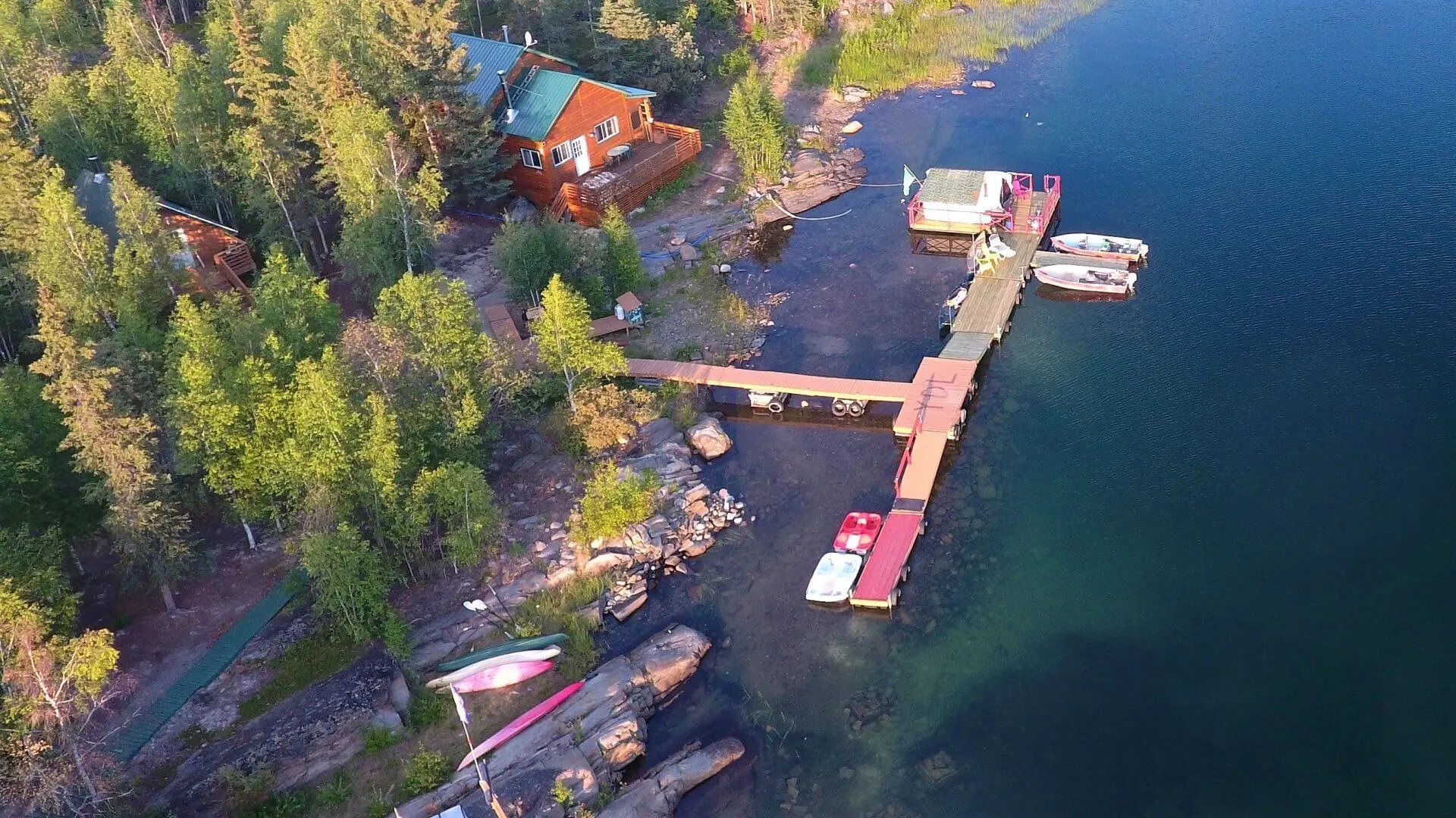 Aerial view of Yellow Dog Lodge buildings and docks on a tree-lined lake shore at golden hour