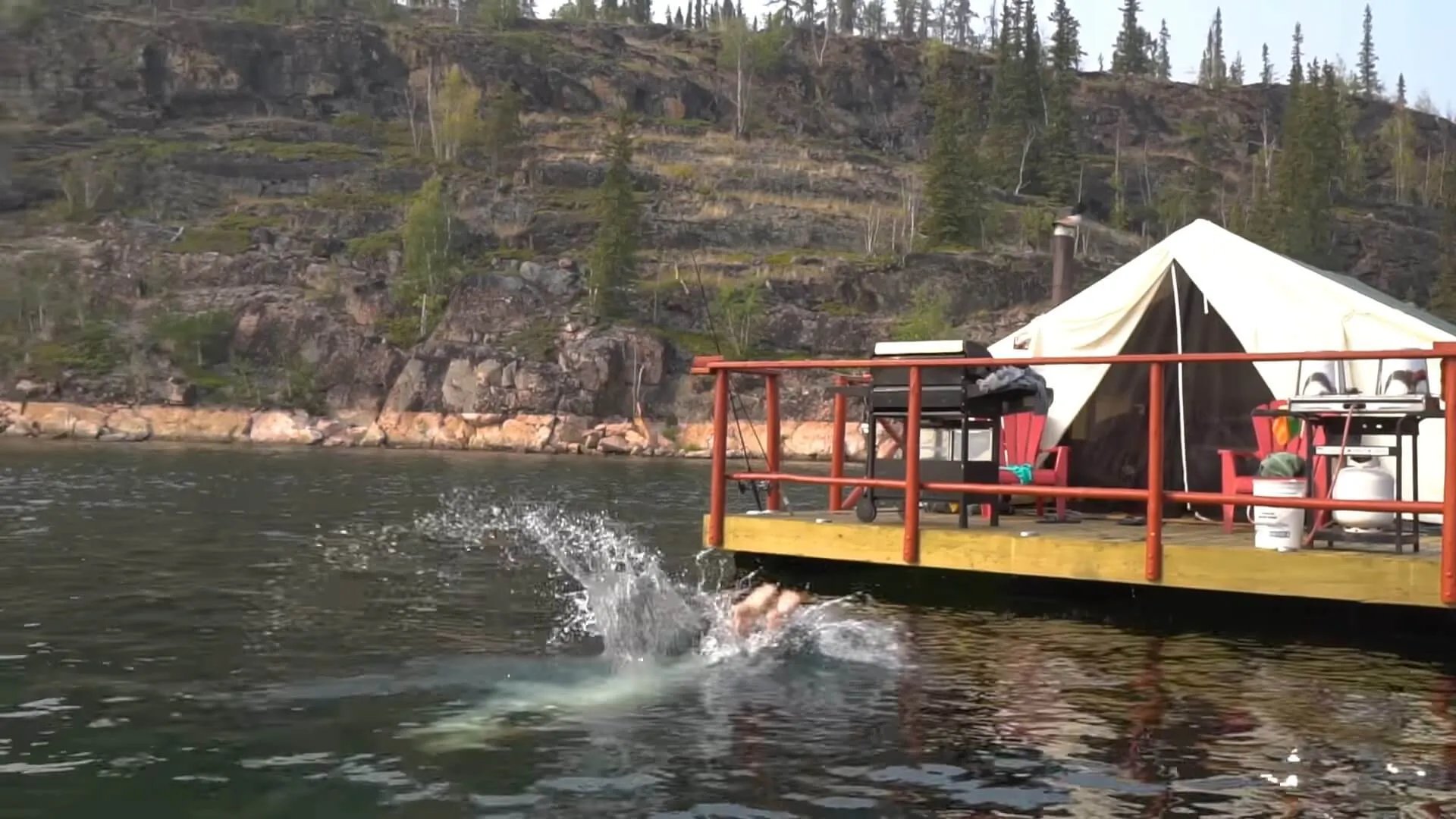Floating tent camp with a person swimming off the side in a bay