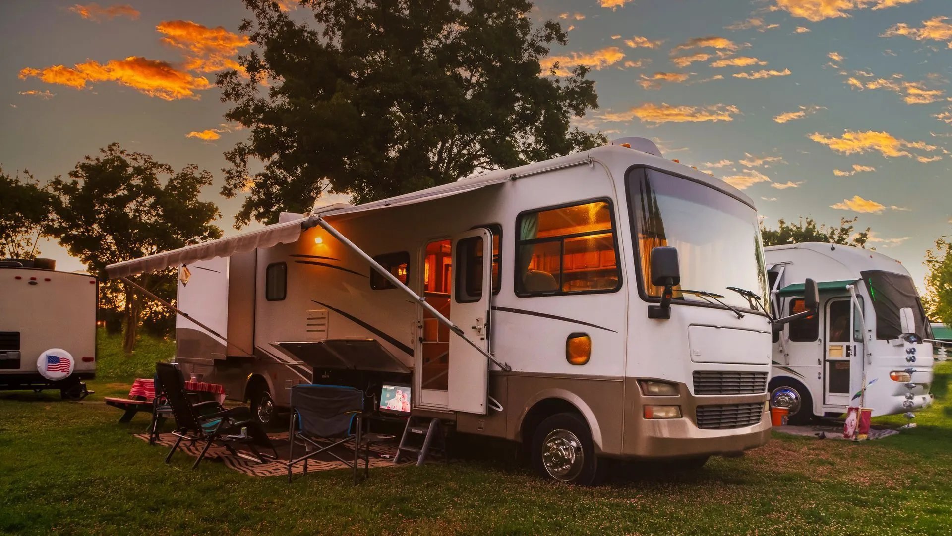 Large RV parked at a campsite with an awning extended, at sunset.