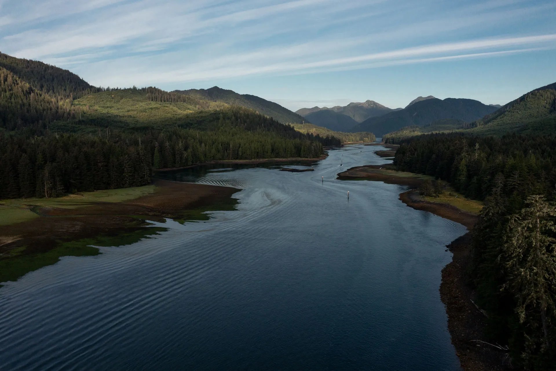 Aerial view of Skidegate Narrows, a winding waterway surrounded by dense green forests under a blue sky.