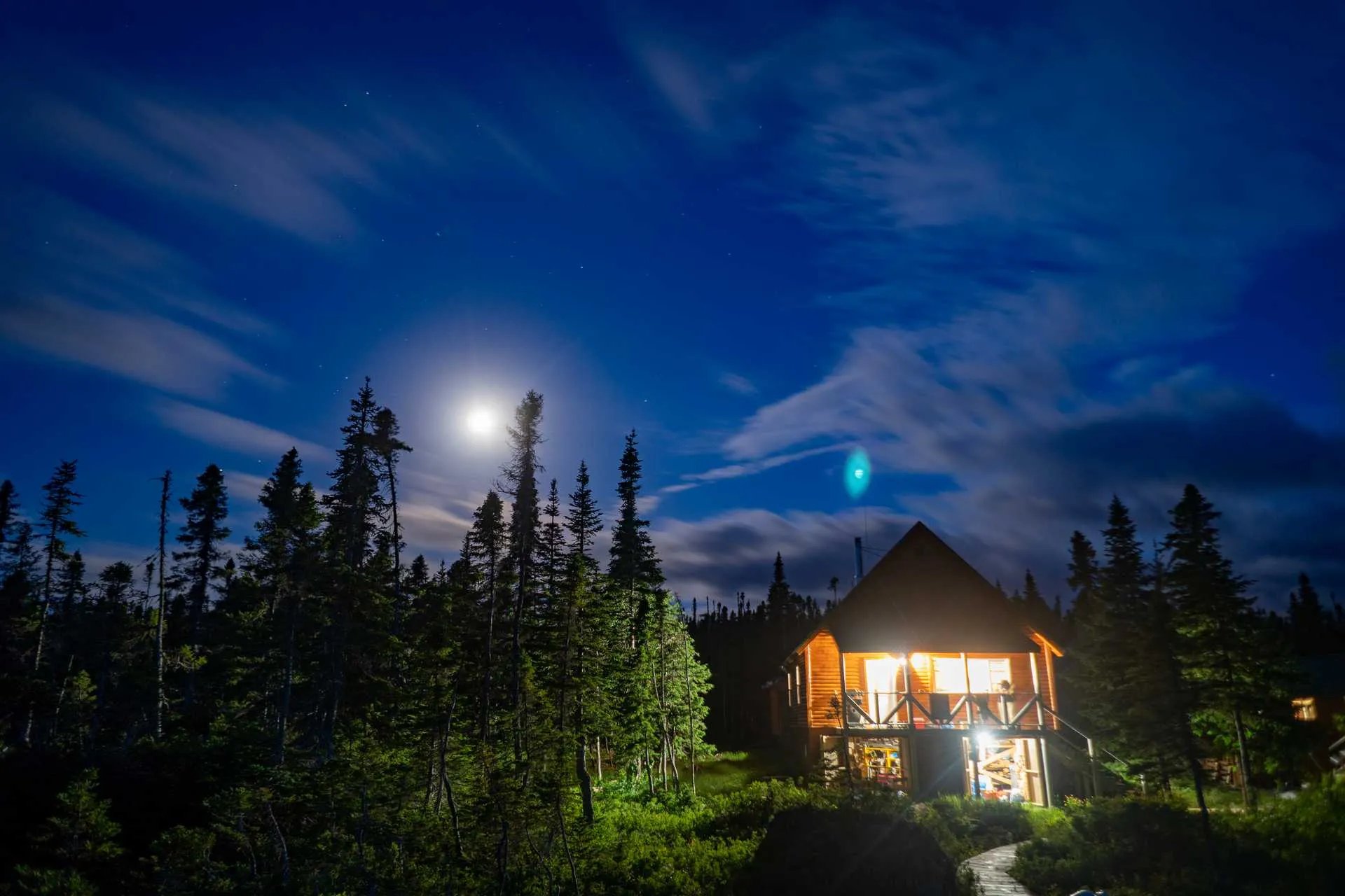 Log cabin lodge illuminated at night under a bright moon and starry sky.