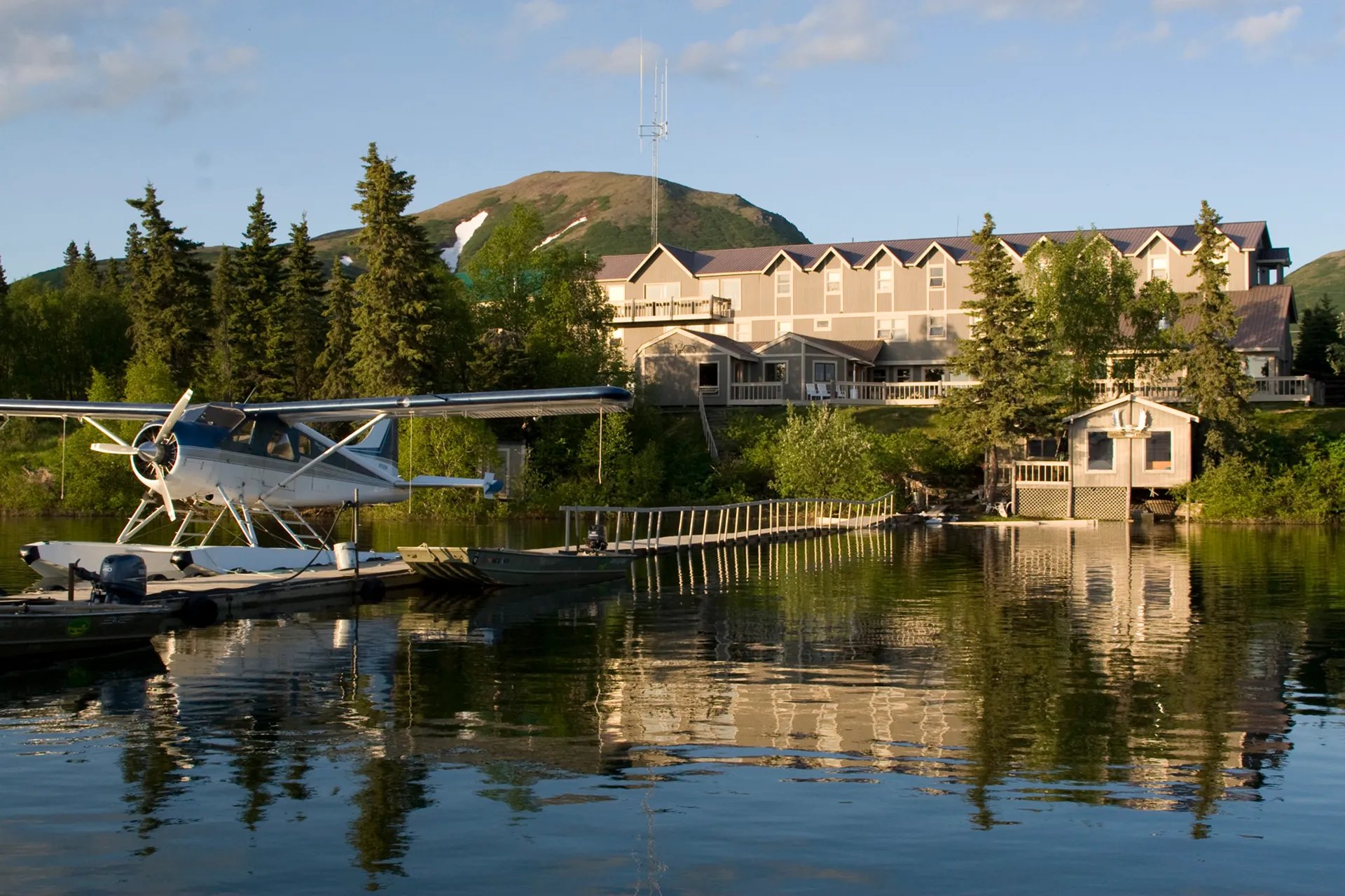 Mission Lodge main building on a lakefront with a floatplane docked, under a clear sky