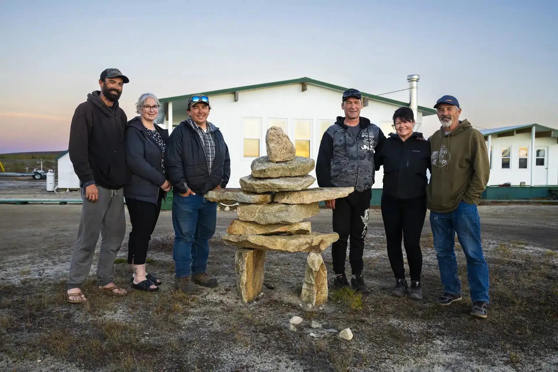Group of people standing around an inukshuk in front of white lodge buildings