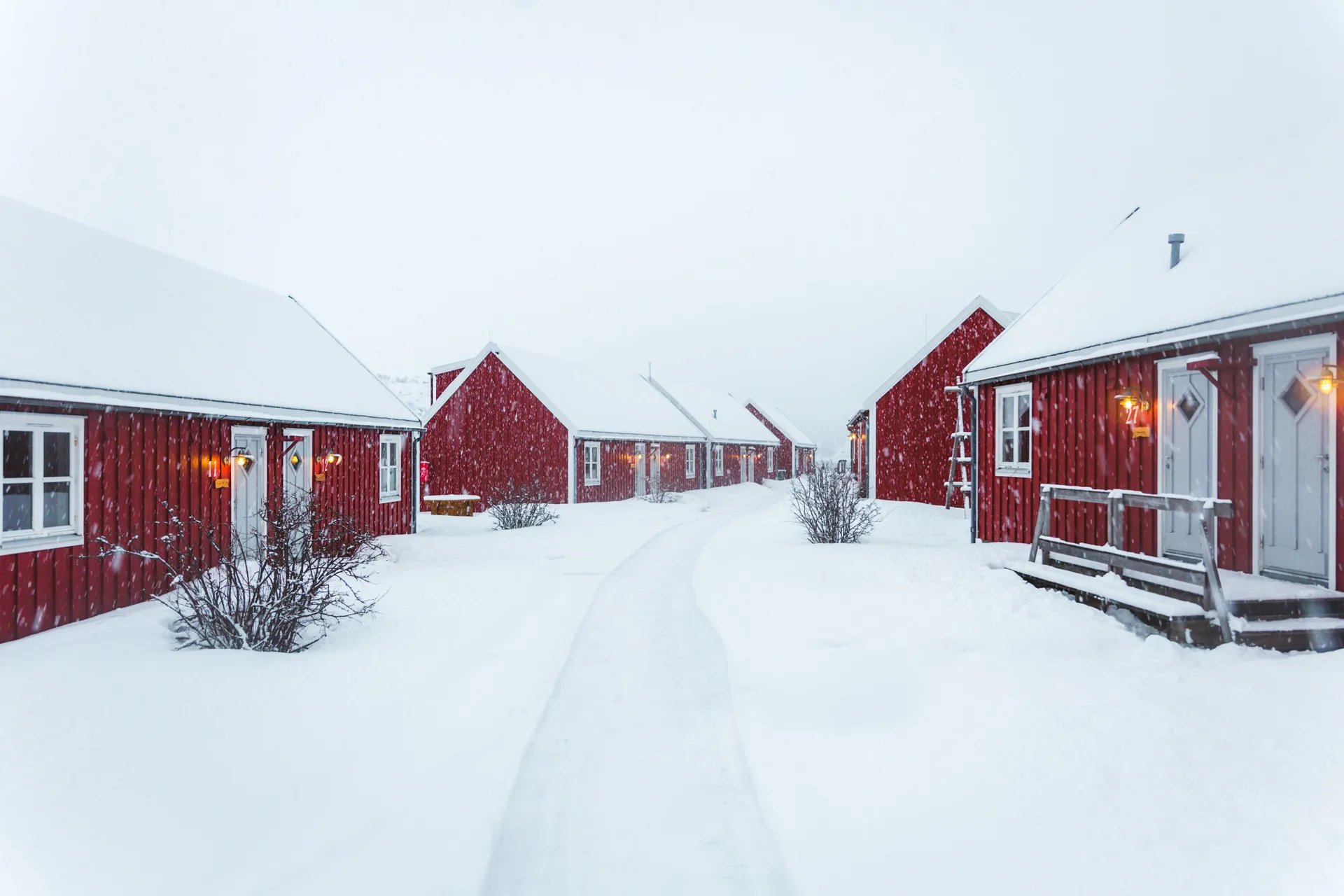 Snow-covered path leading between traditional red cabins in winter