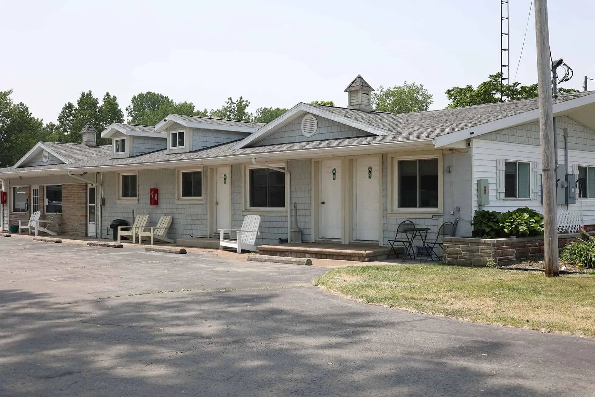 Exterior of a light-blue motel building with multiple rooms and white Adirondack chairs on the porch