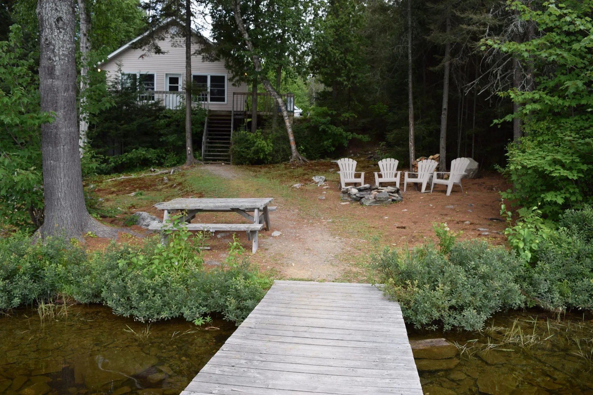 Rustic cabin with a dock and fire pit area by a serene lake.