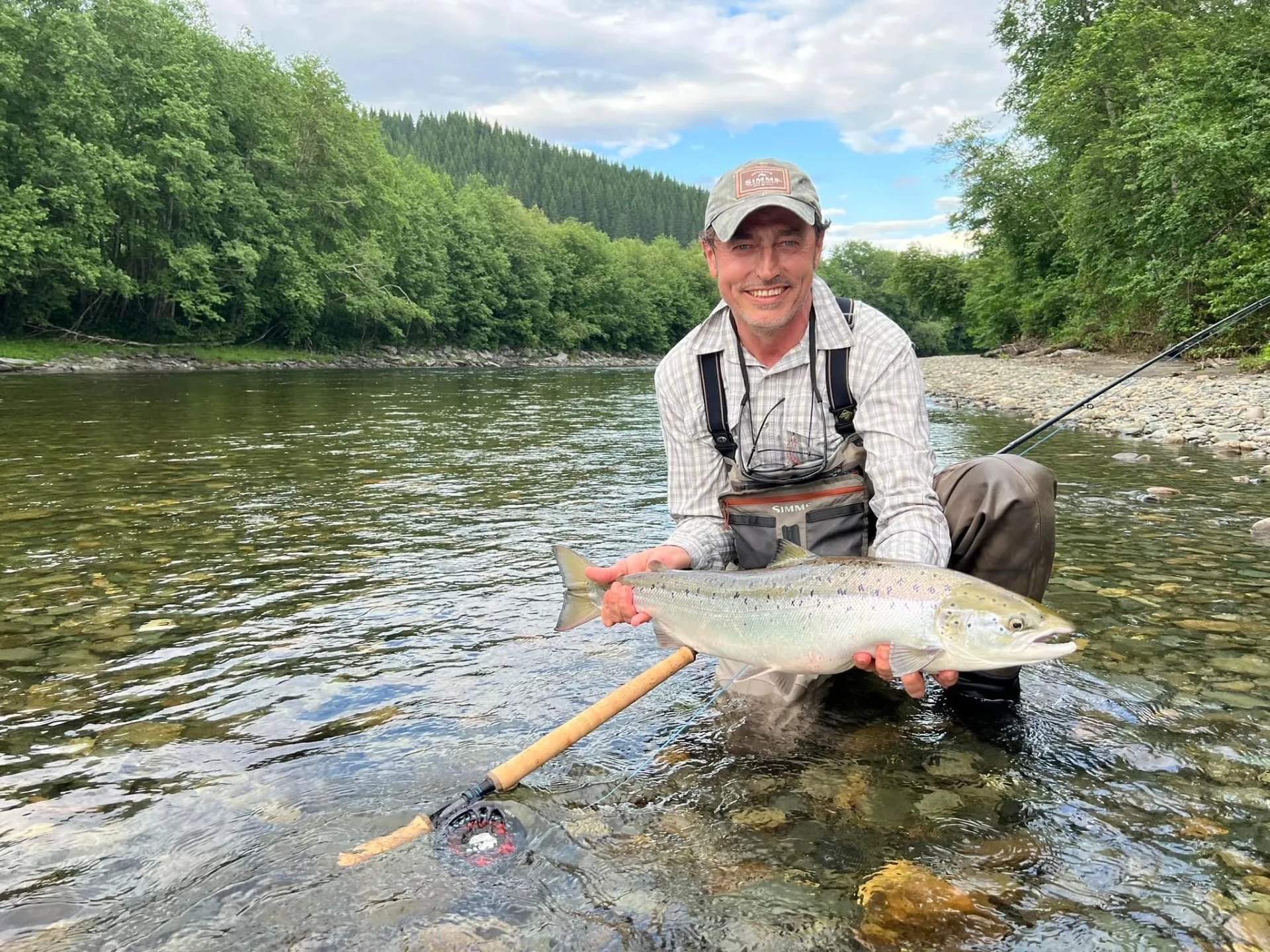 Angler in waders holding a large silver Atlantic salmon in the river