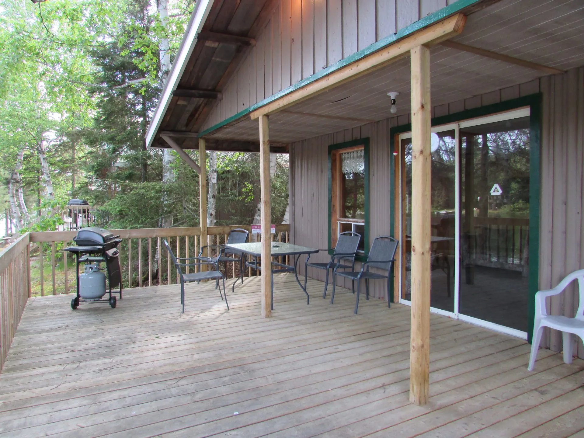 Wooden deck of a cabin with a barbecue grill and an outdoor dining set.