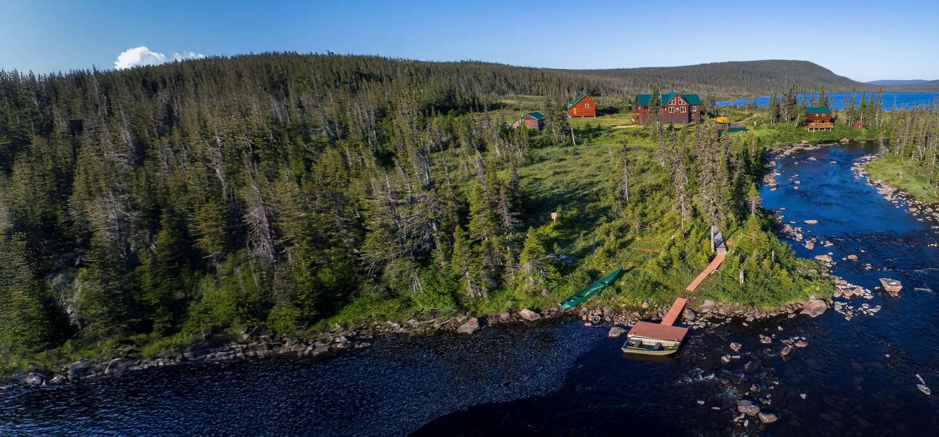 Panoramic aerial view of the Arluk Outfitters lodge compound by a large lake and river.