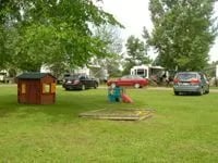 Small wooden playhouse and sandbox in a grassy campground area.