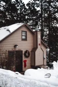 Cozy cabin exterior in winter with a snow-dusted wreath on the door and a red stocking.
