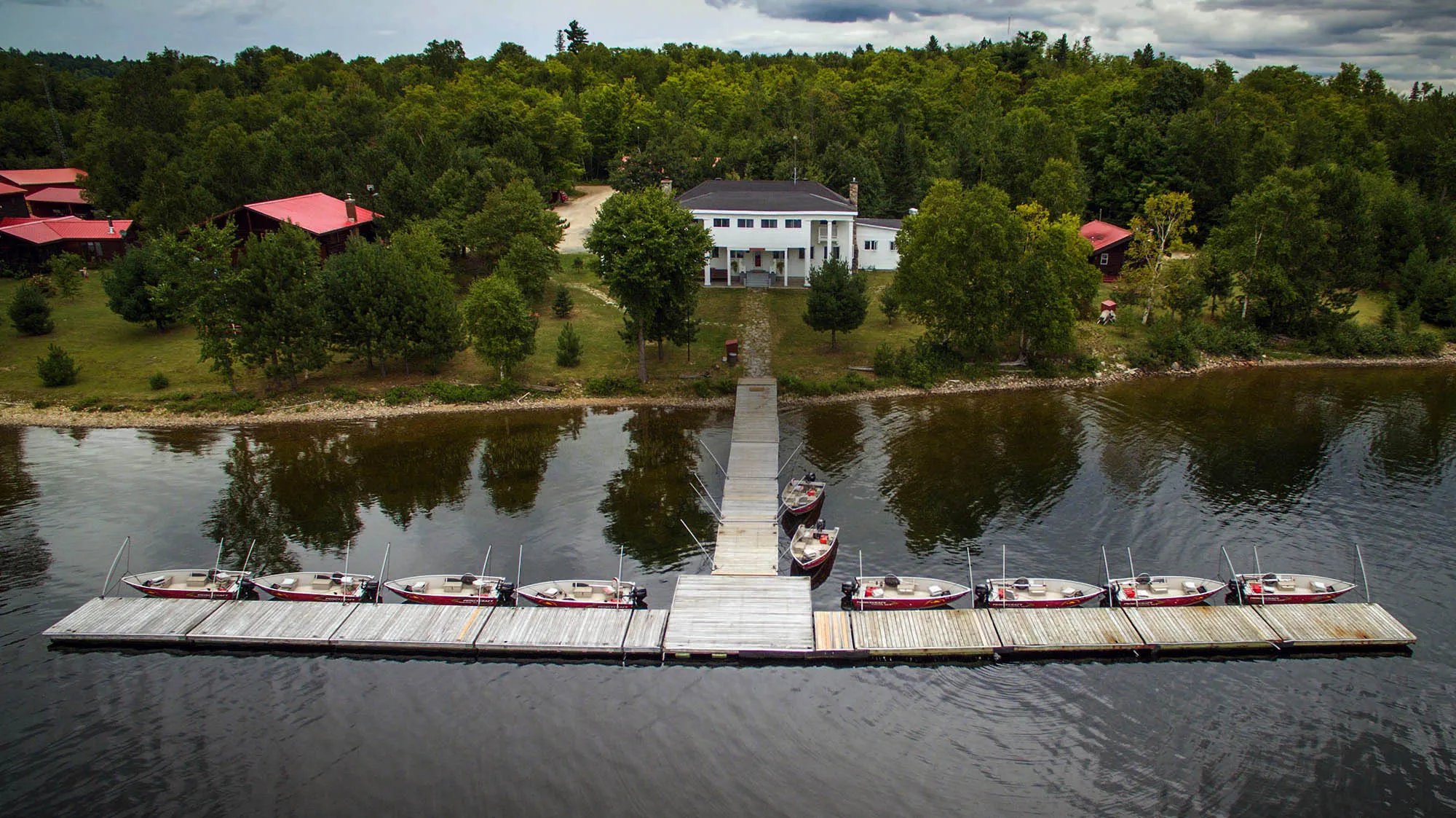 Aerial view of the white main lodge, long dock, and boats on the lake