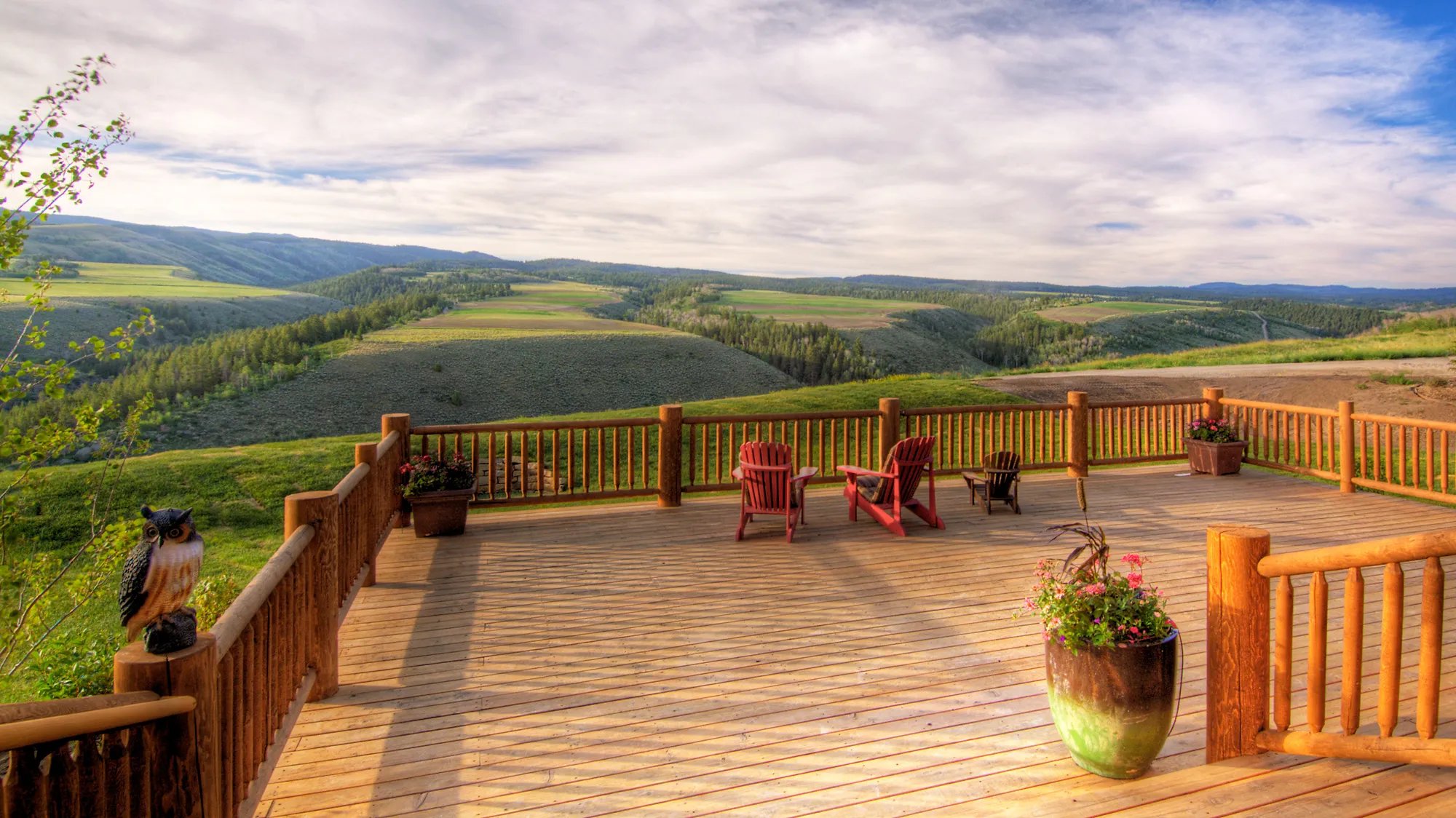 Expansive wooden deck with Adirondack chairs overlooking a green valley and rolling hills