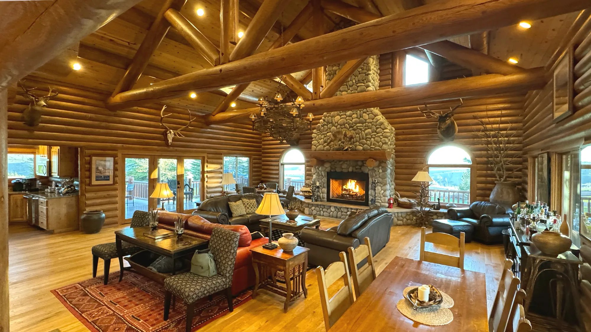 Rustic log lodge great room with a large stone fireplace, exposed beams, and comfortable seating