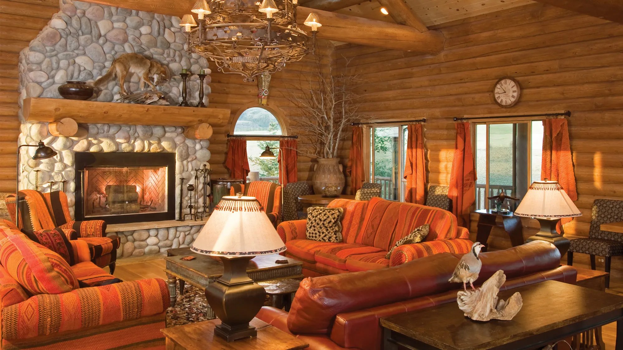 Cozy log cabin living area with a stone fireplace, orange sofas, and rustic decor