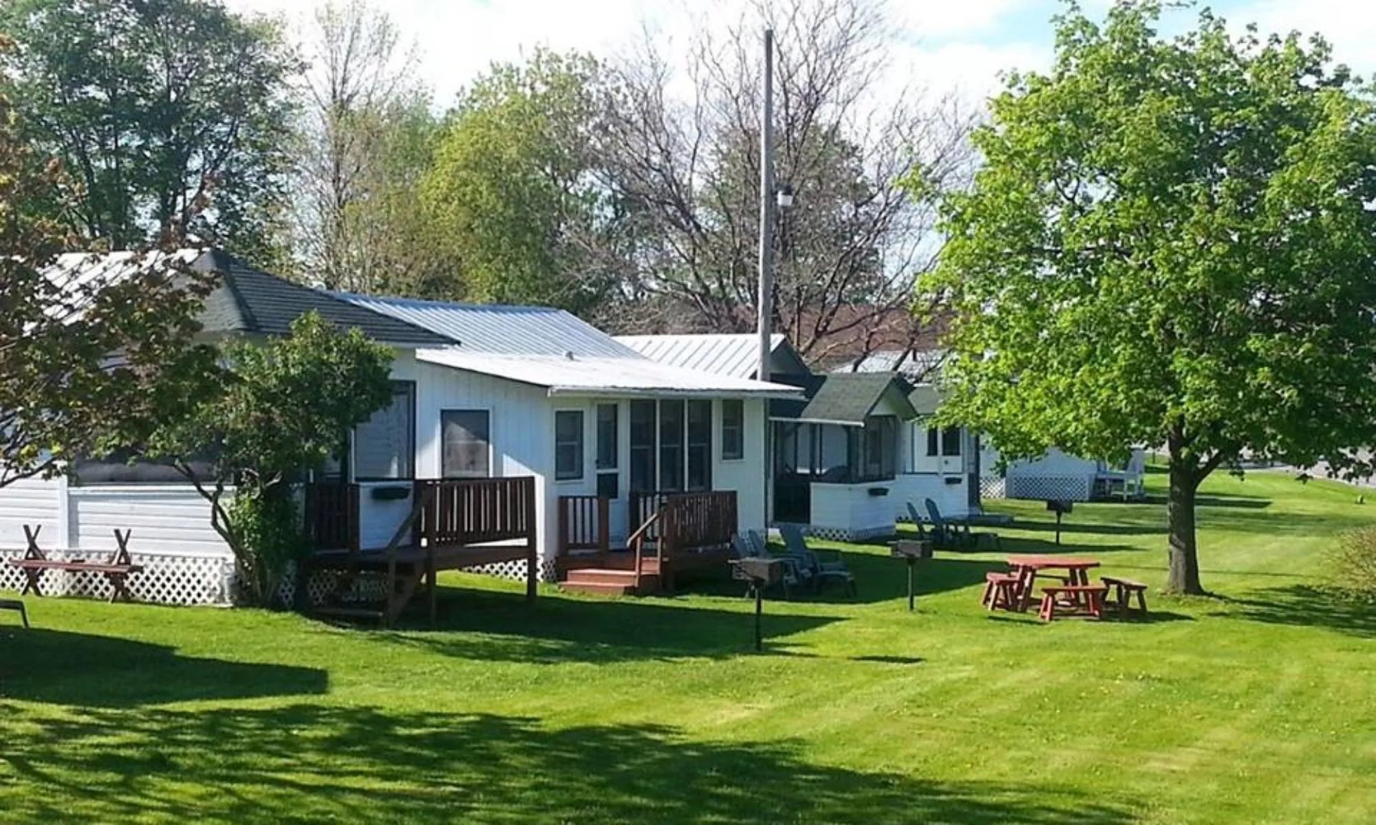 Row of white cabins with green roofs and screened porches on a sunny green lawn
