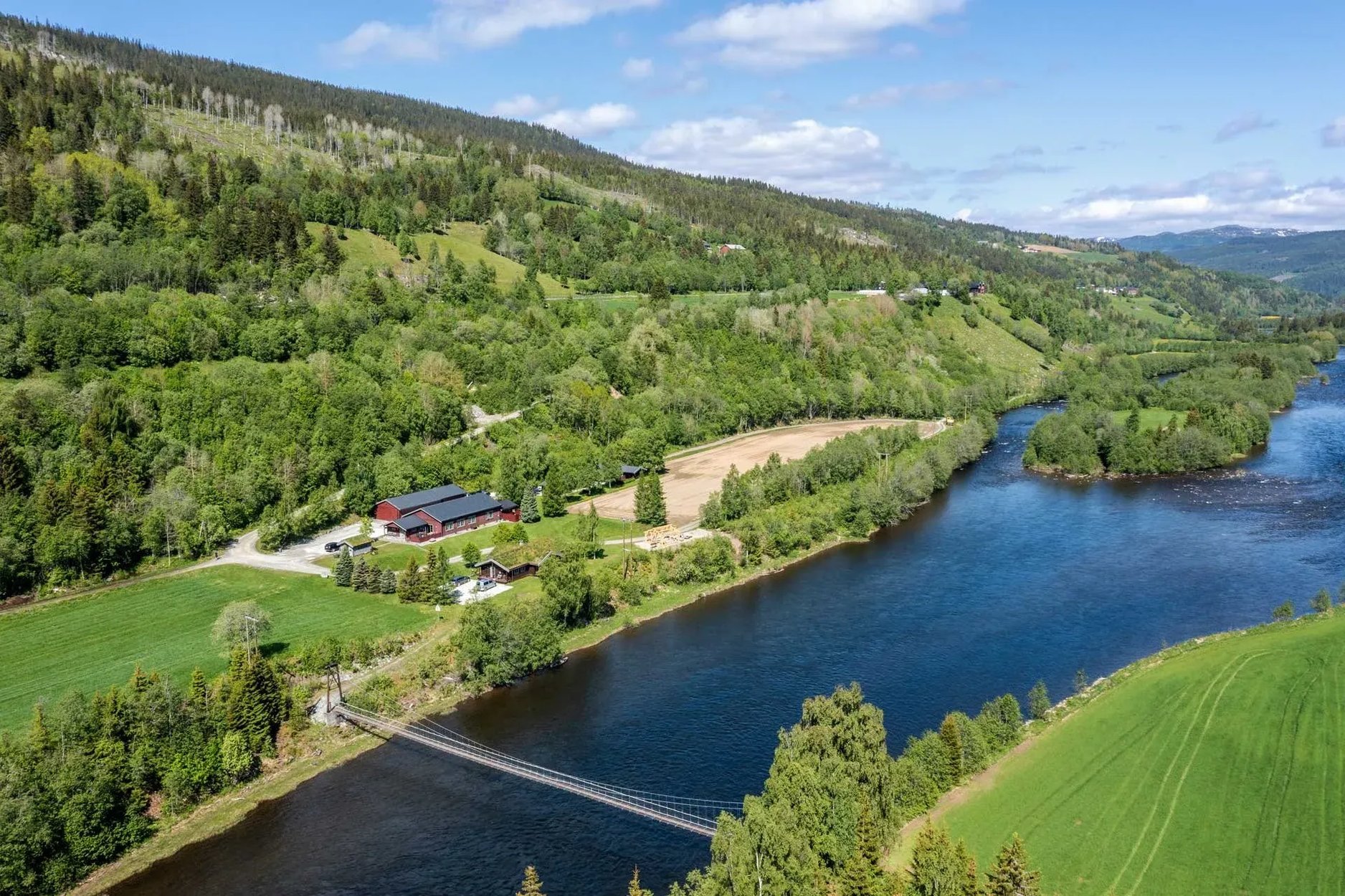 Aerial view of a river winding through green agricultural fields and forests under a clear sky.