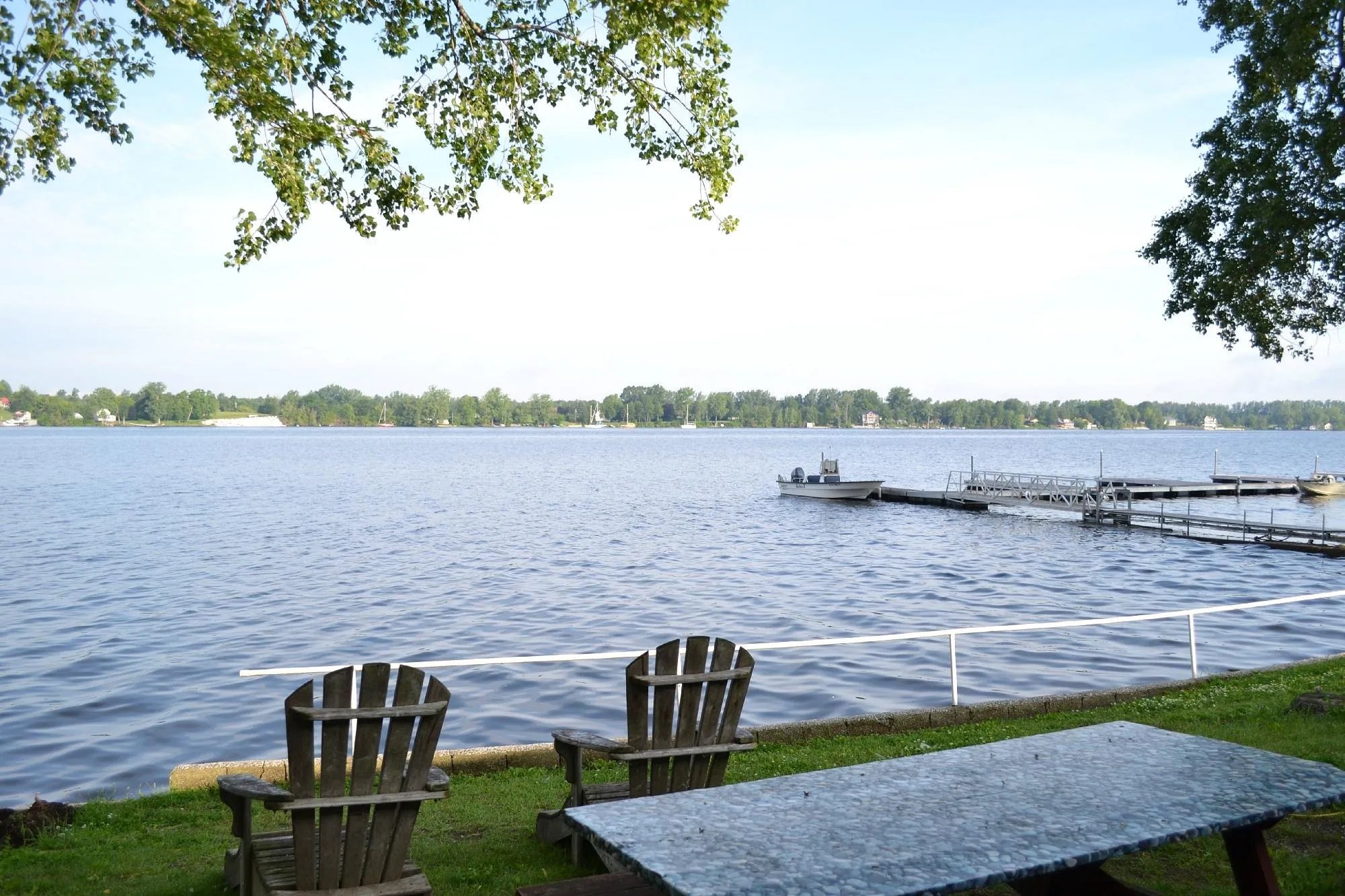 Lakefront view with two Adirondack chairs, a picnic table, and a dock in the distance