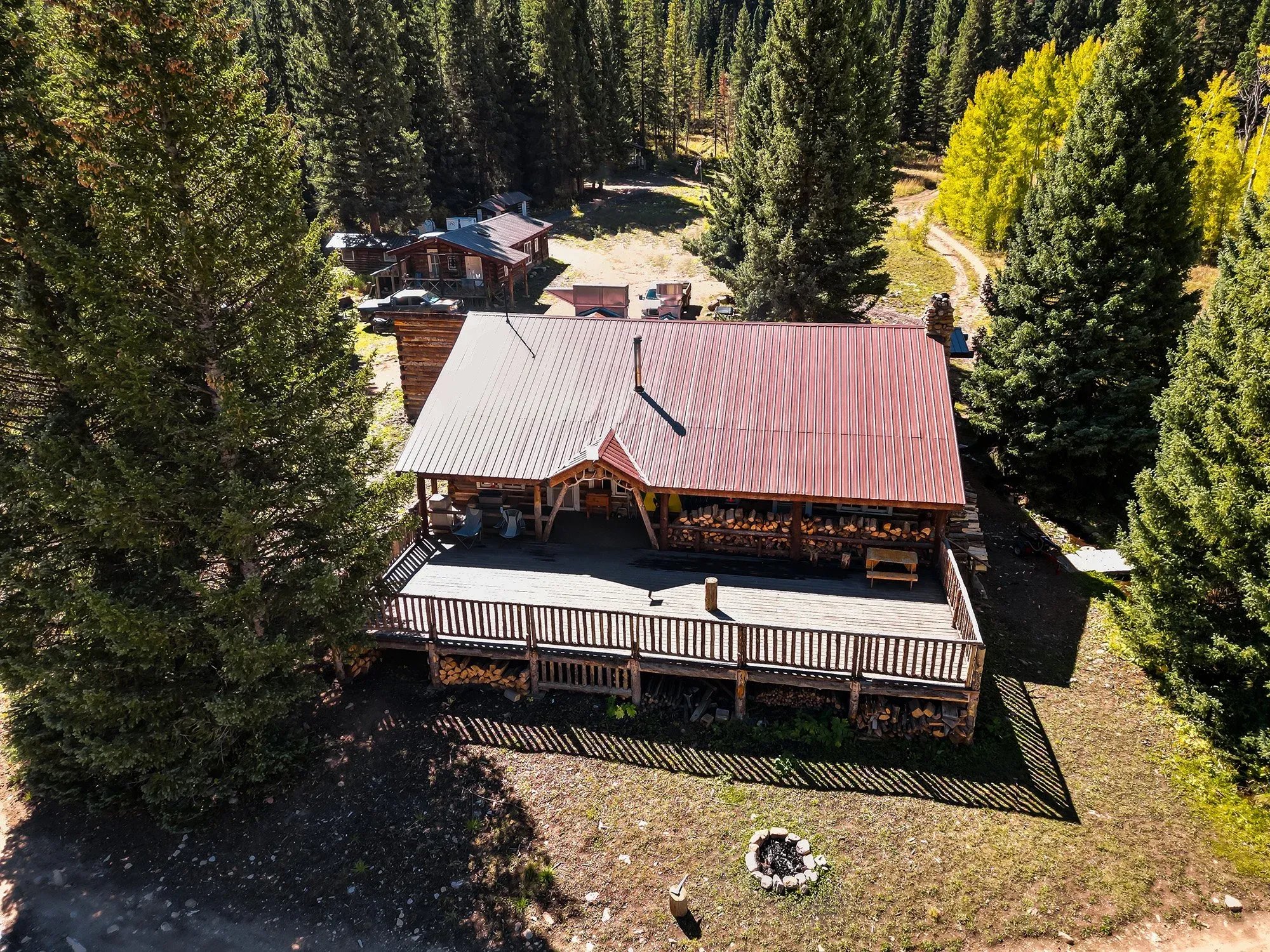 Aerial view of a rustic log lodge with a red roof and large deck, surrounded by pine trees.