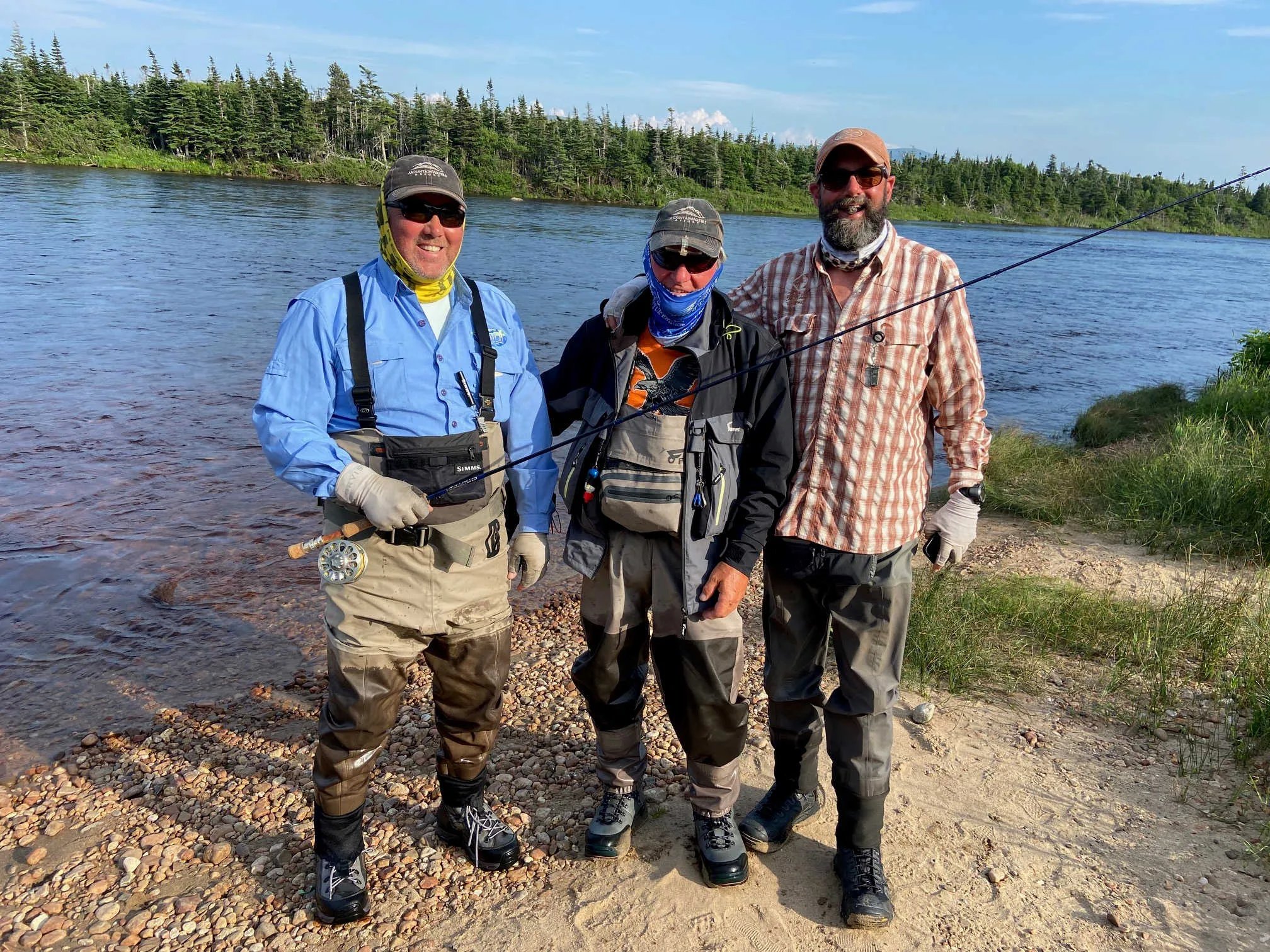 Three anglers in waders posing on a sunny riverbank