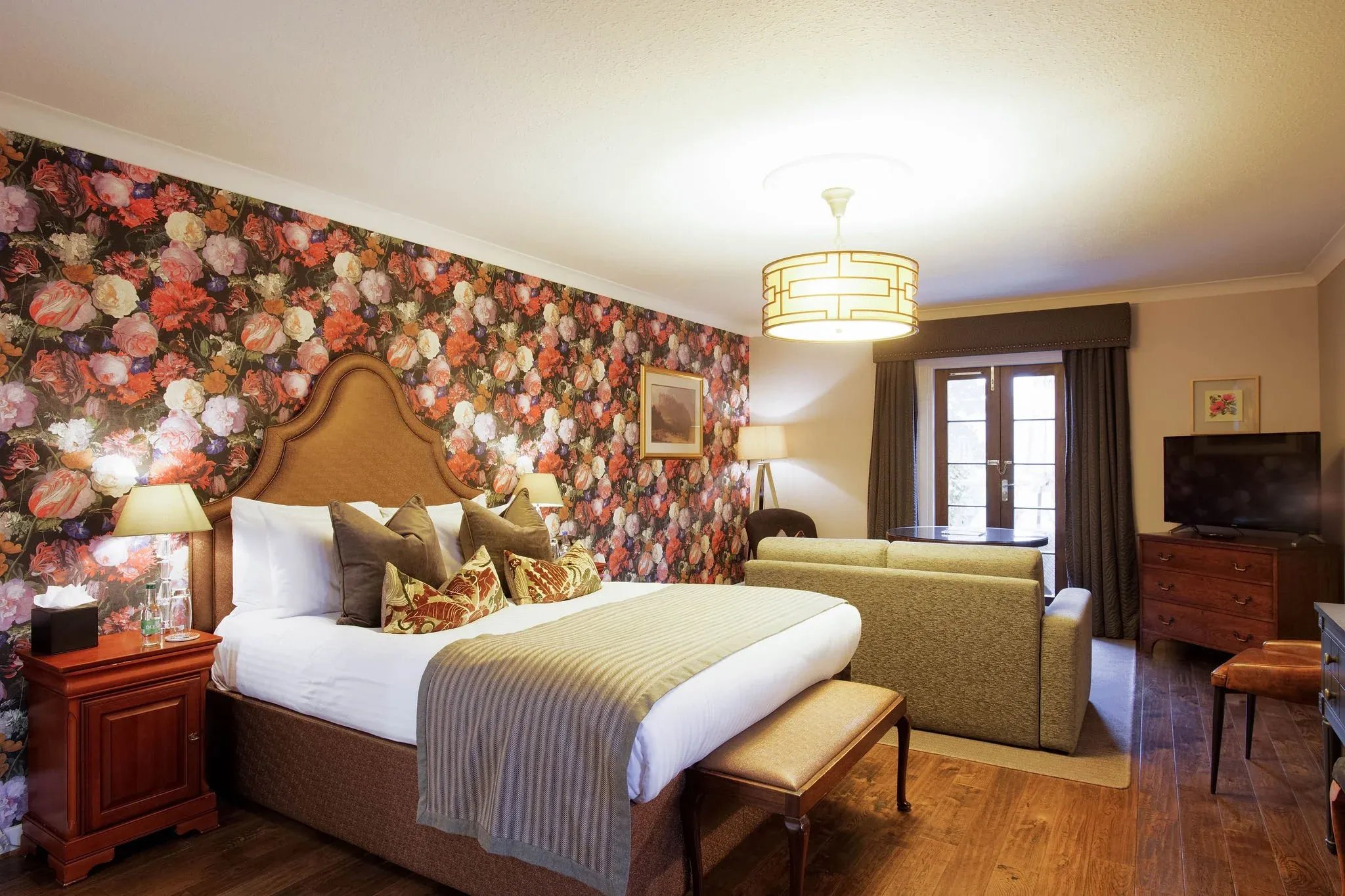 Bedroom with a large bed, floral wallpaper accent wall, and a sofa