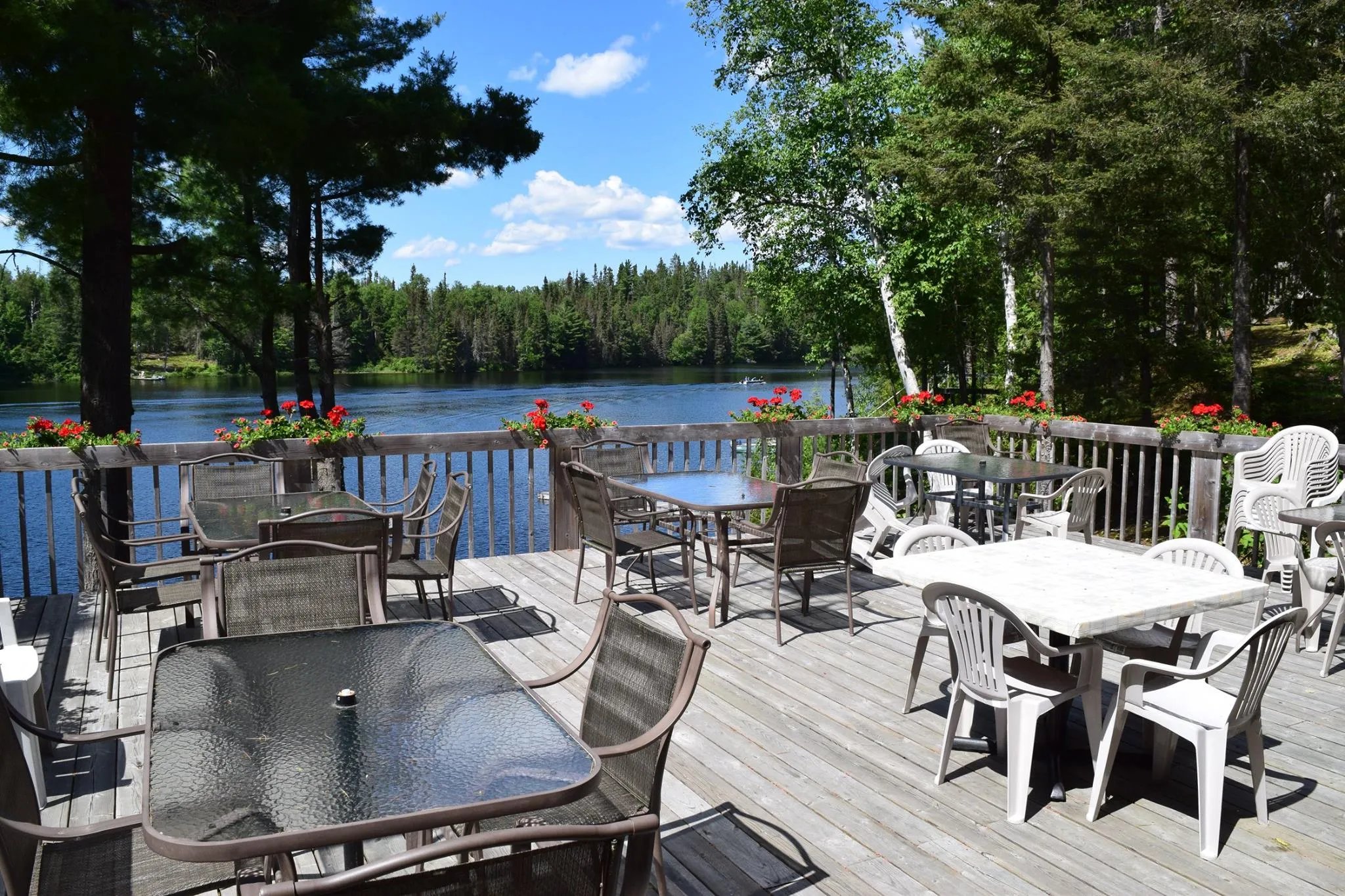 Spacious outdoor dining deck with tables and chairs overlooking a lake on a sunny day.