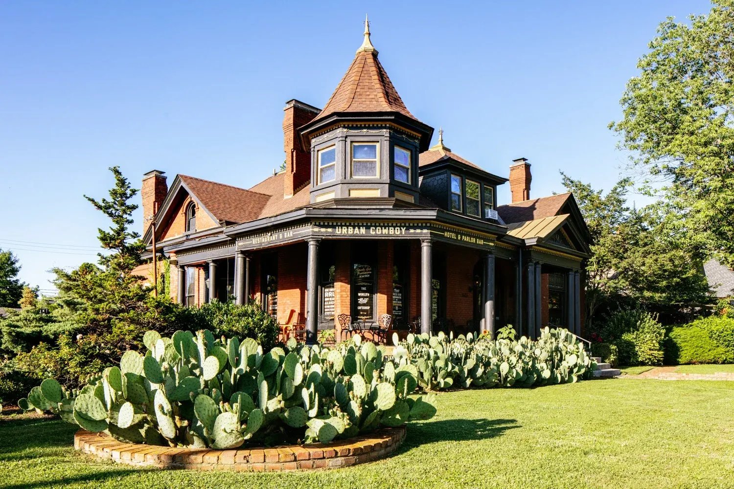 Grand Victorian-style house with people gathered on a green lawn at dusk.