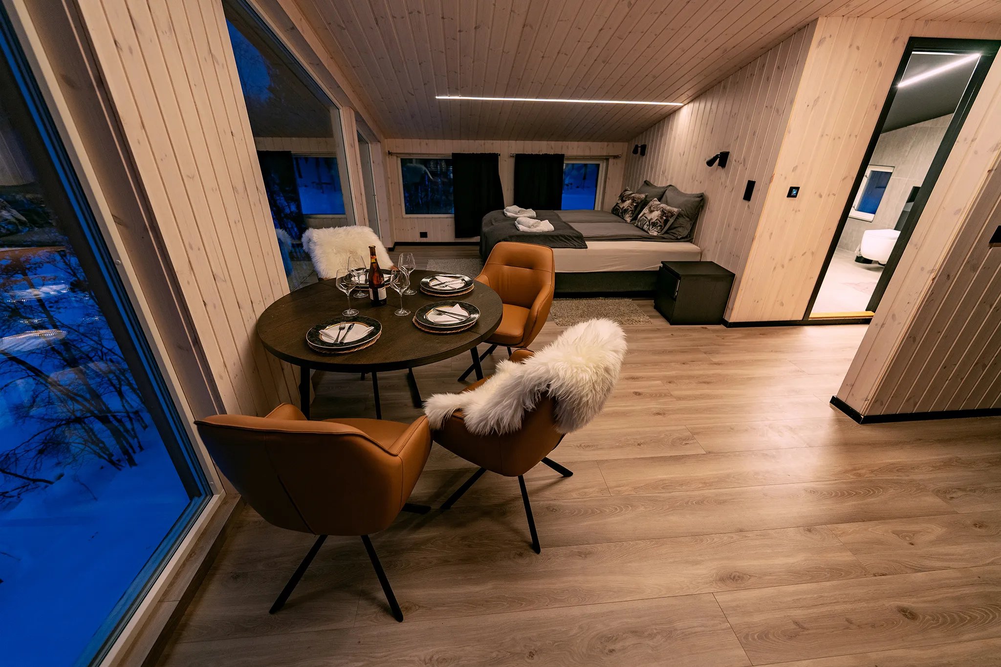 Modern Mollis suite interior with a dining table, chairs, and a bed in the background.