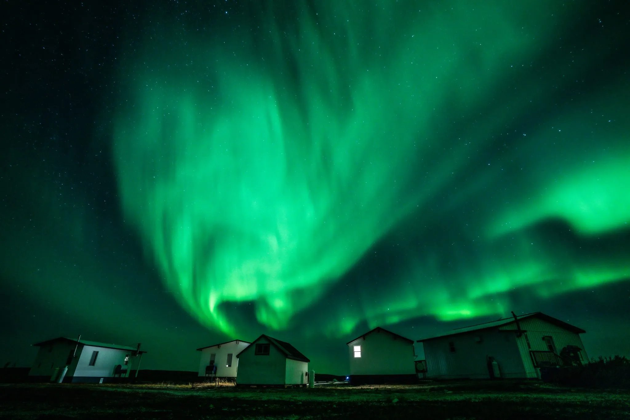 Vibrant green aurora borealis swirling over white cabins at night
