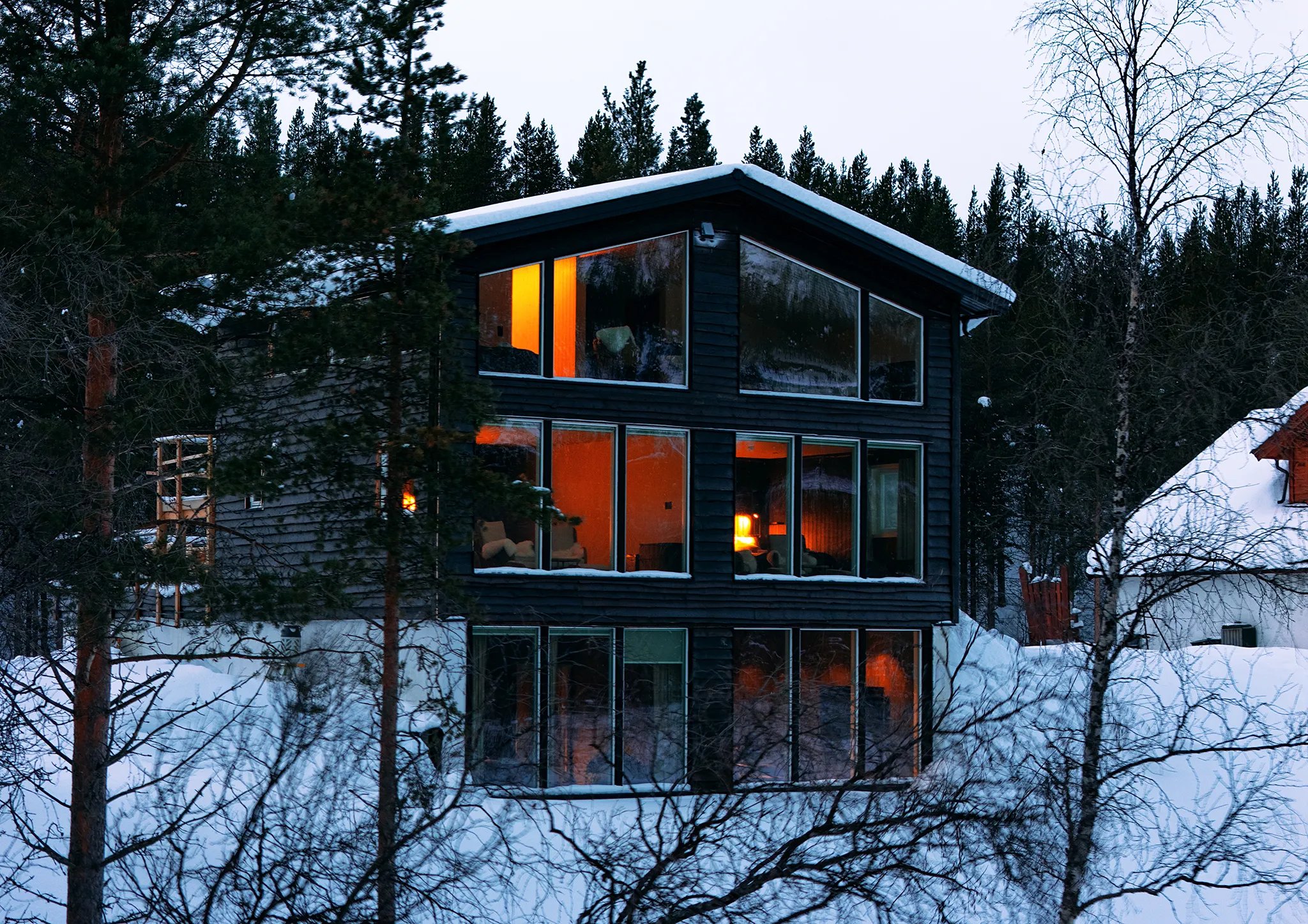 Aerial view of two modern lodge buildings glowing warmly at dusk in a snowy landscape.