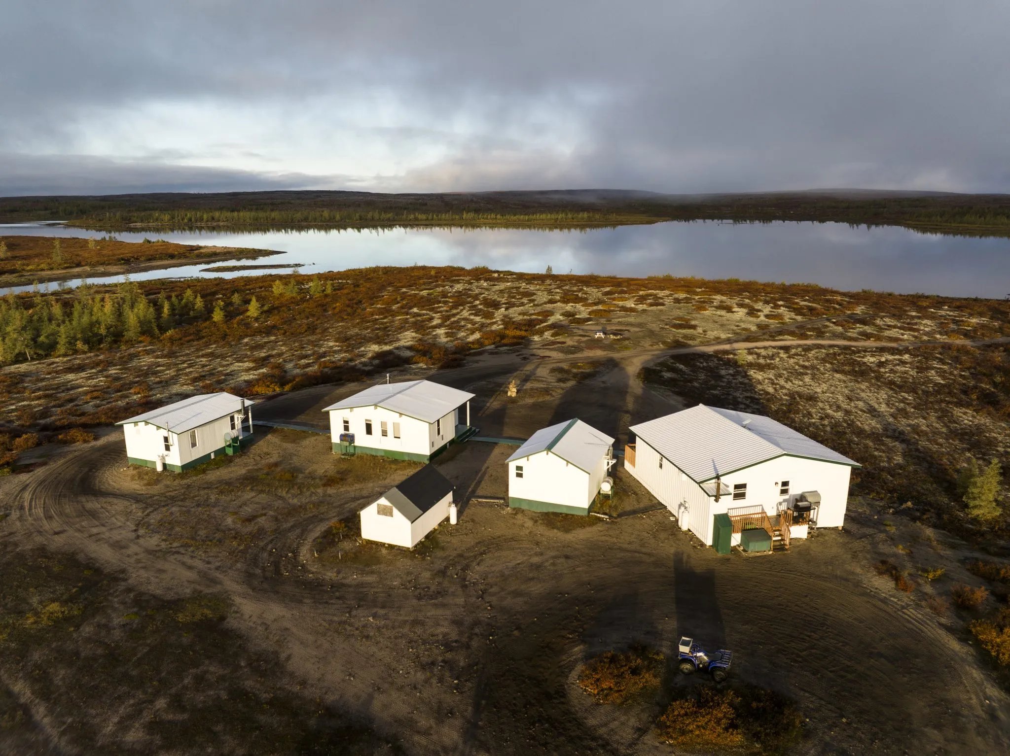 Aerial view of white cabins scattered across a tundra landscape beside a lake