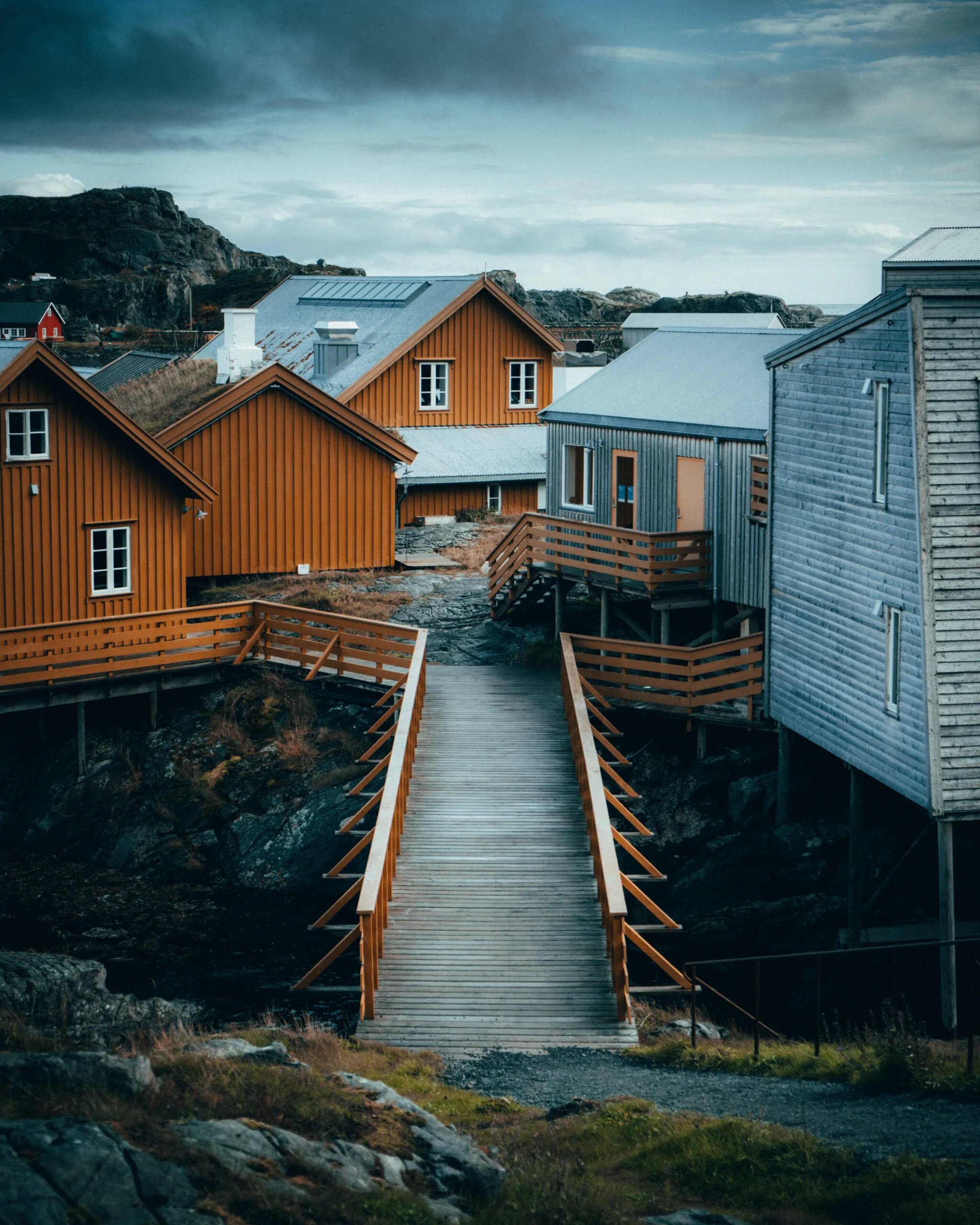 Wooden walkways connecting traditional and modern cabins on a rocky shore with mountains.