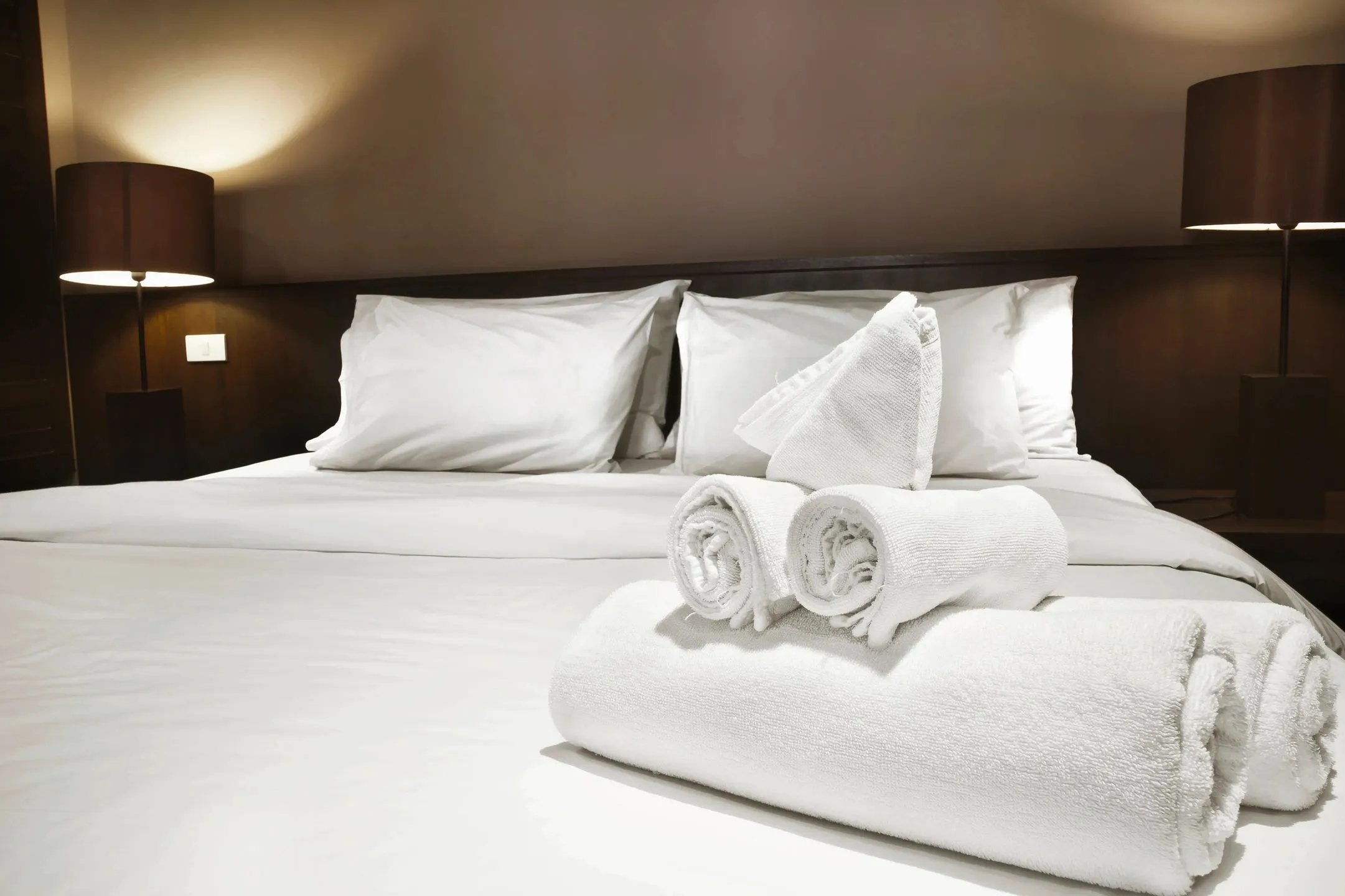 King-size bed with white linens and rolled white towels, bedside lamps lit