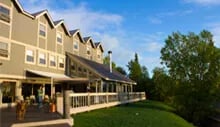 Mission Lodge building with a long covered deck overlooking a green lawn under a blue sky.