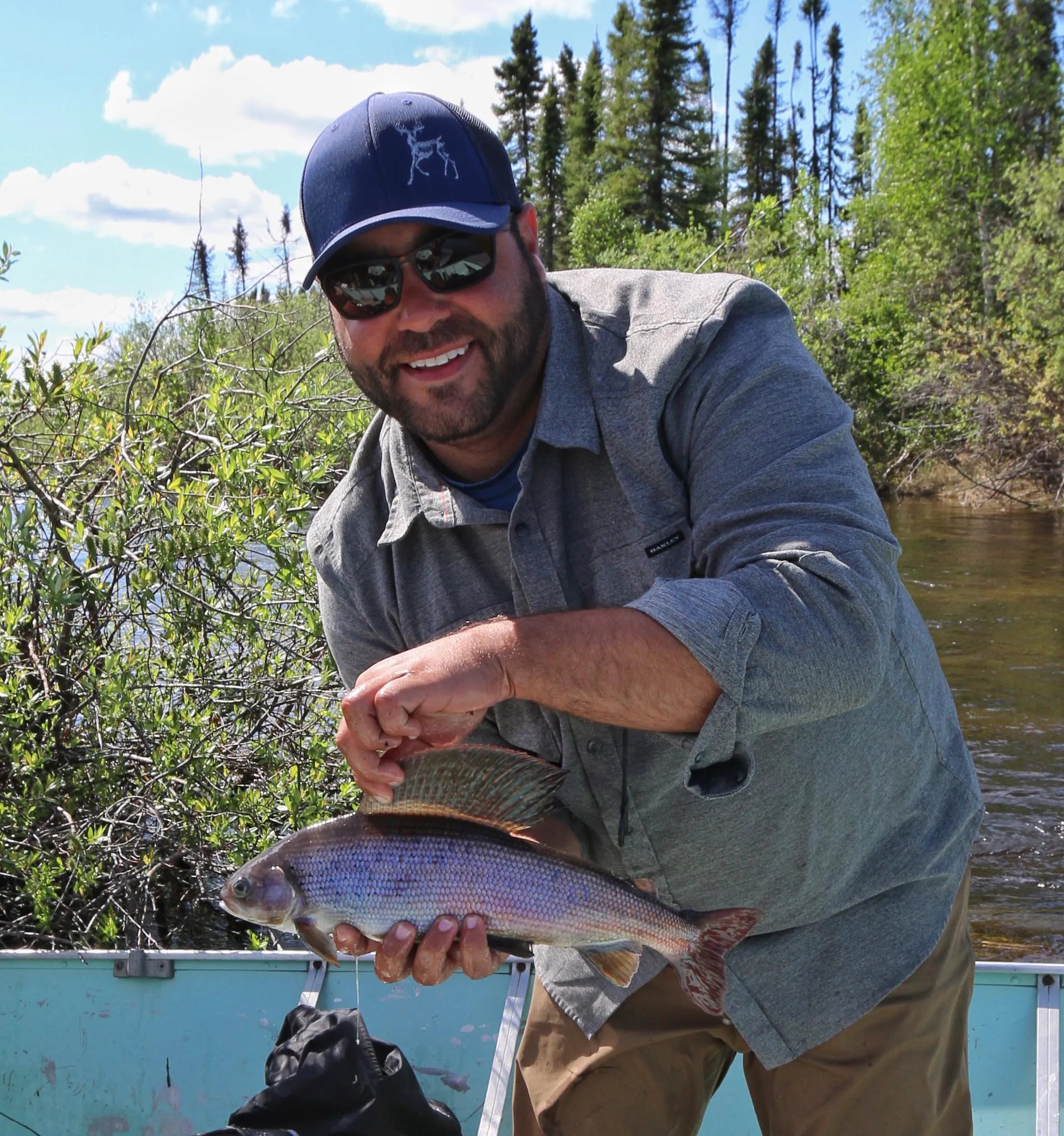 Smiling angler holding an Arctic Grayling in a boat with trees in the background