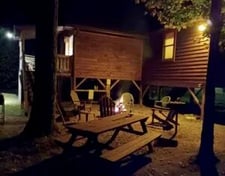 Rustic cabin with a porch, partially obscured by vibrant orange and yellow fall foliage