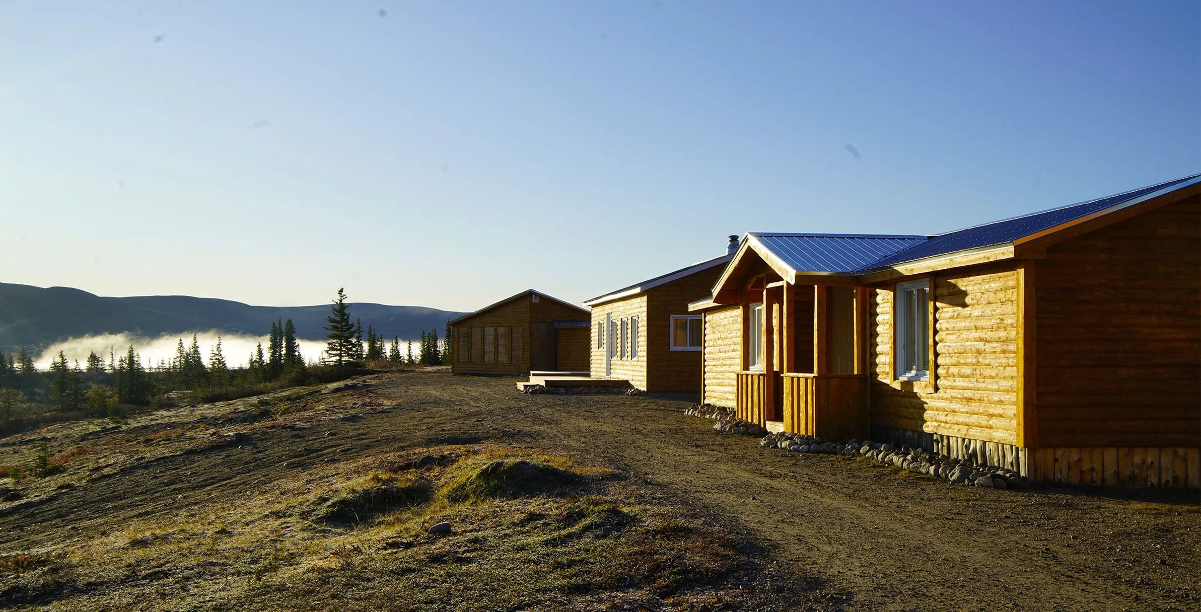 Wooden lodge buildings on a hill with a misty valley in the background