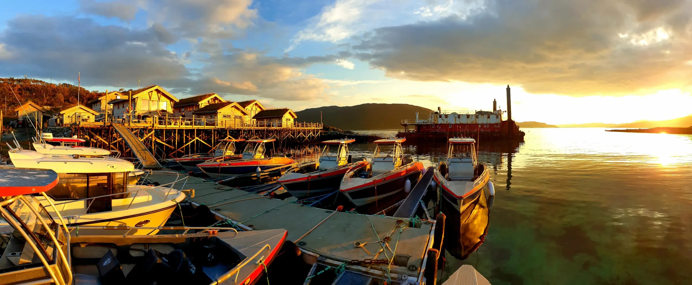 Panoramic view of lodge buildings with a hot tub and sauna hut on a sunny day by the water