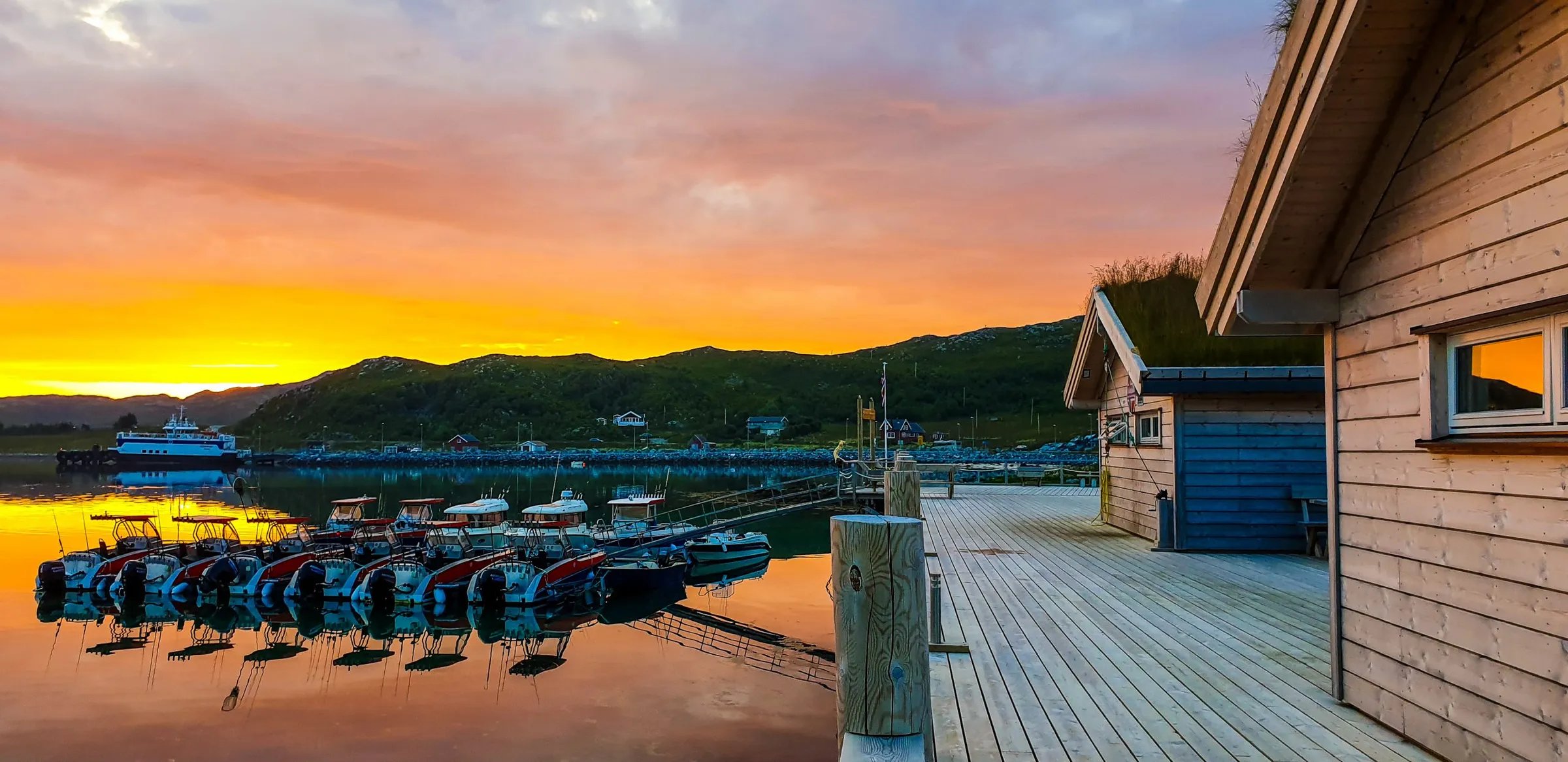 Boats docked at a pier next to lodge buildings at sunset, with an orange sky