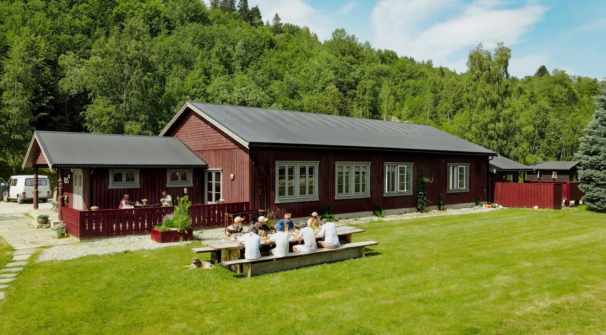 Red wooden main lodge building with a dark roof, green lawn, and outdoor picnic tables.