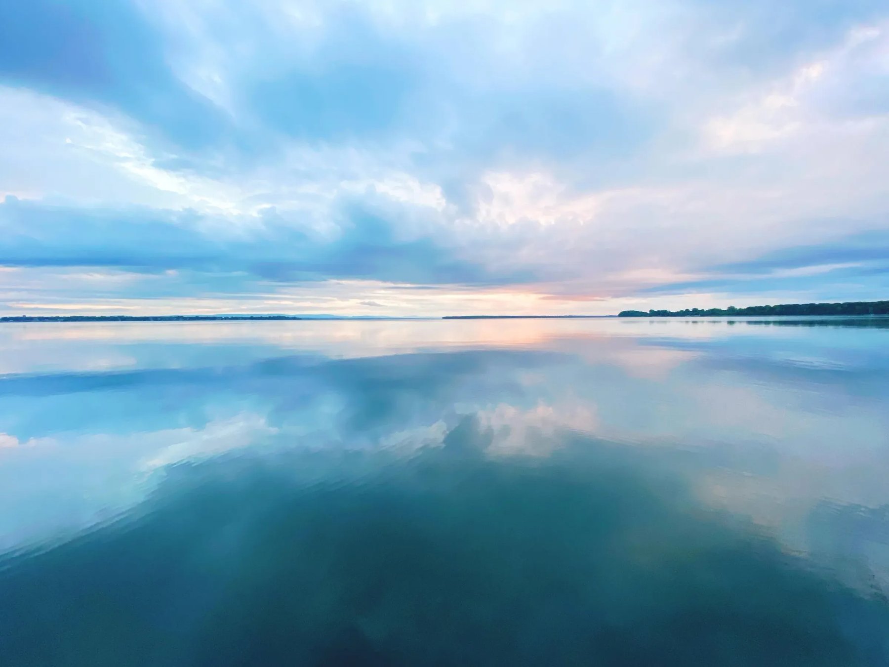 Aerial view of a forested peninsula extending into a large lake under a colorful sunset sky