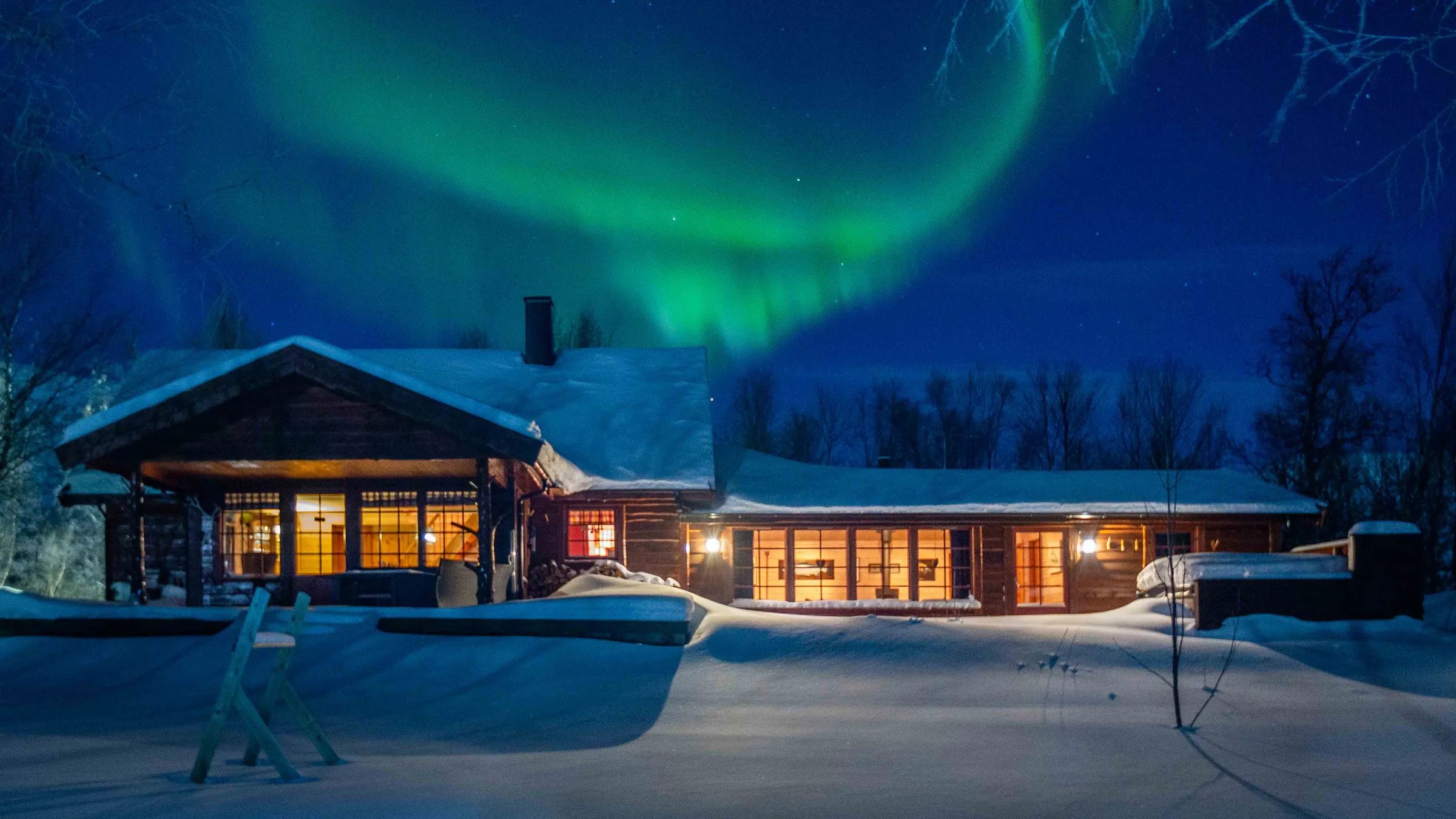 Snow-covered lodge exterior illuminated at night under vibrant green Northern Lights