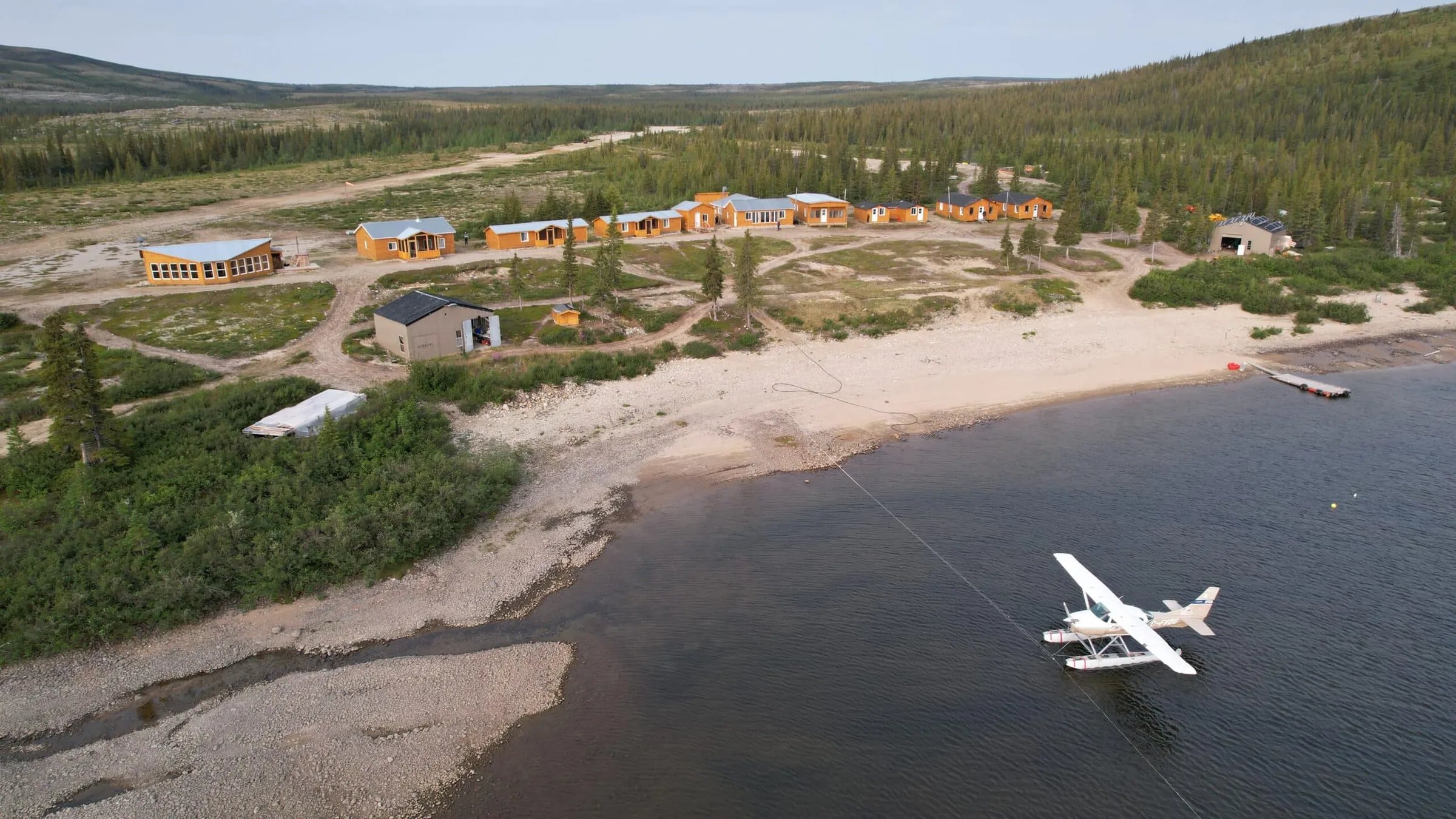 Aerial view of the lodge compound with multiple cabins and a floatplane on the water