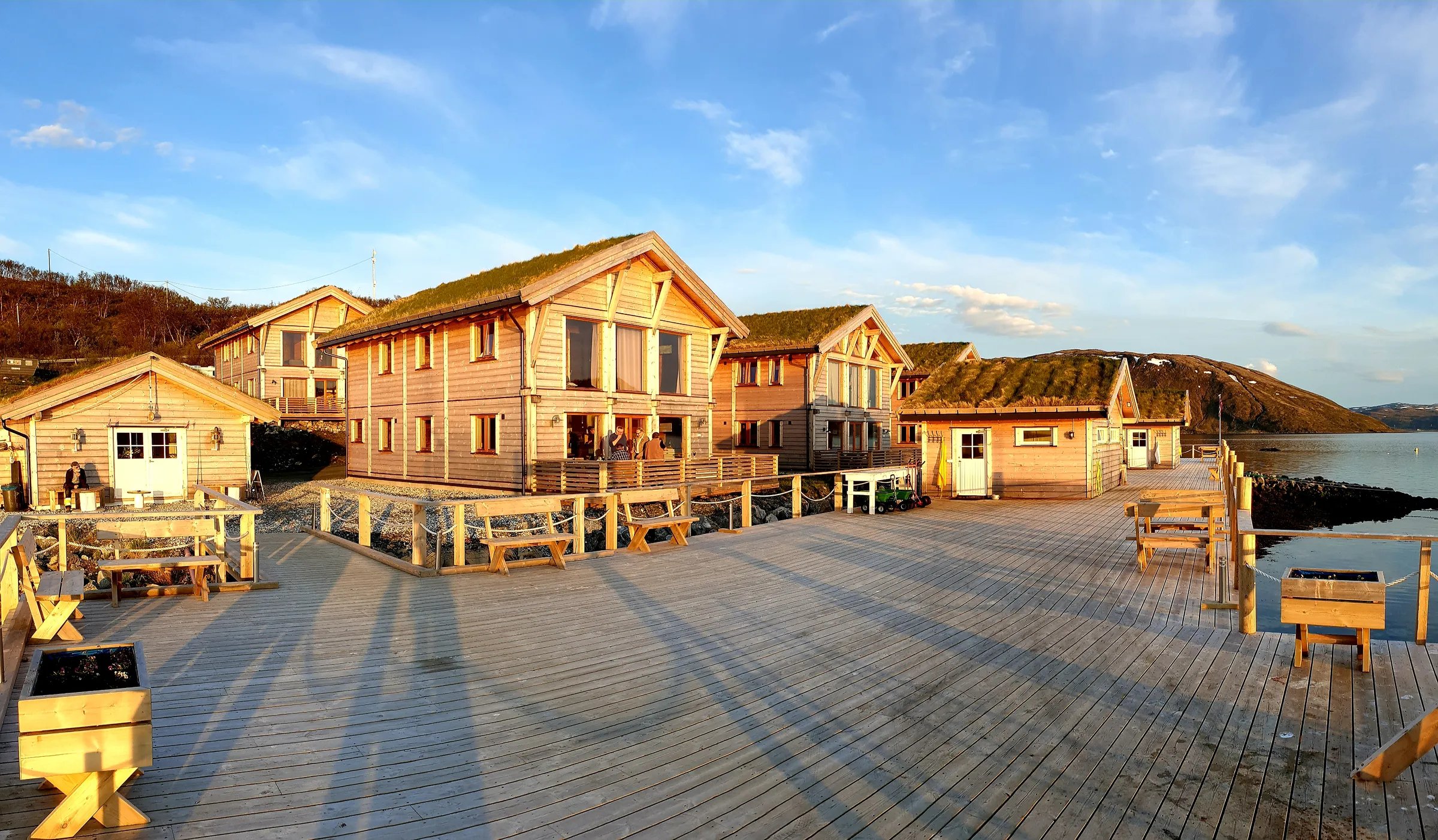 Lodge buildings with green roofs on a wooden pier extending into the water at sunset