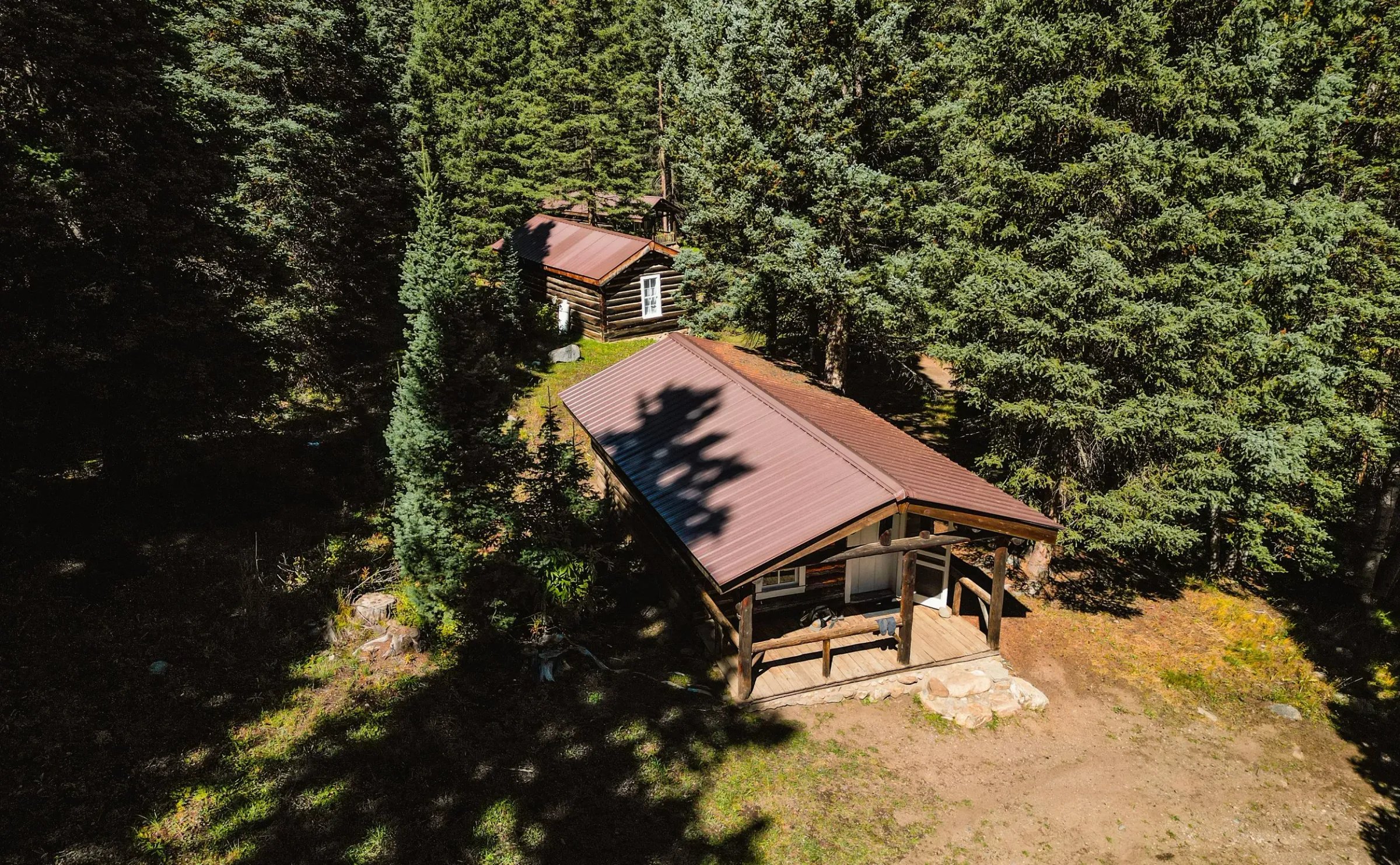Aerial view of two log cabins with brown roofs nestled among dense evergreen trees.